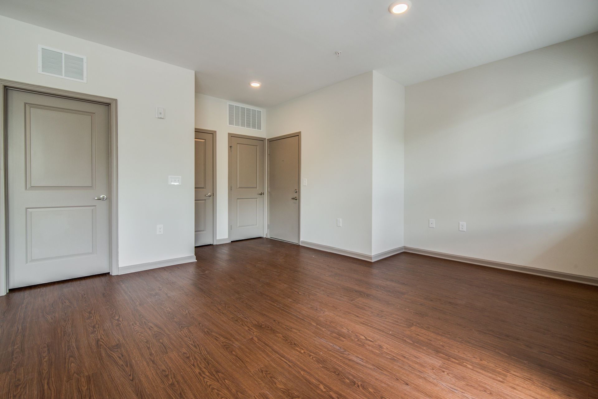 Empty room with brown wood-look floor, white walls, and three tan doors at Marvel Apartments.