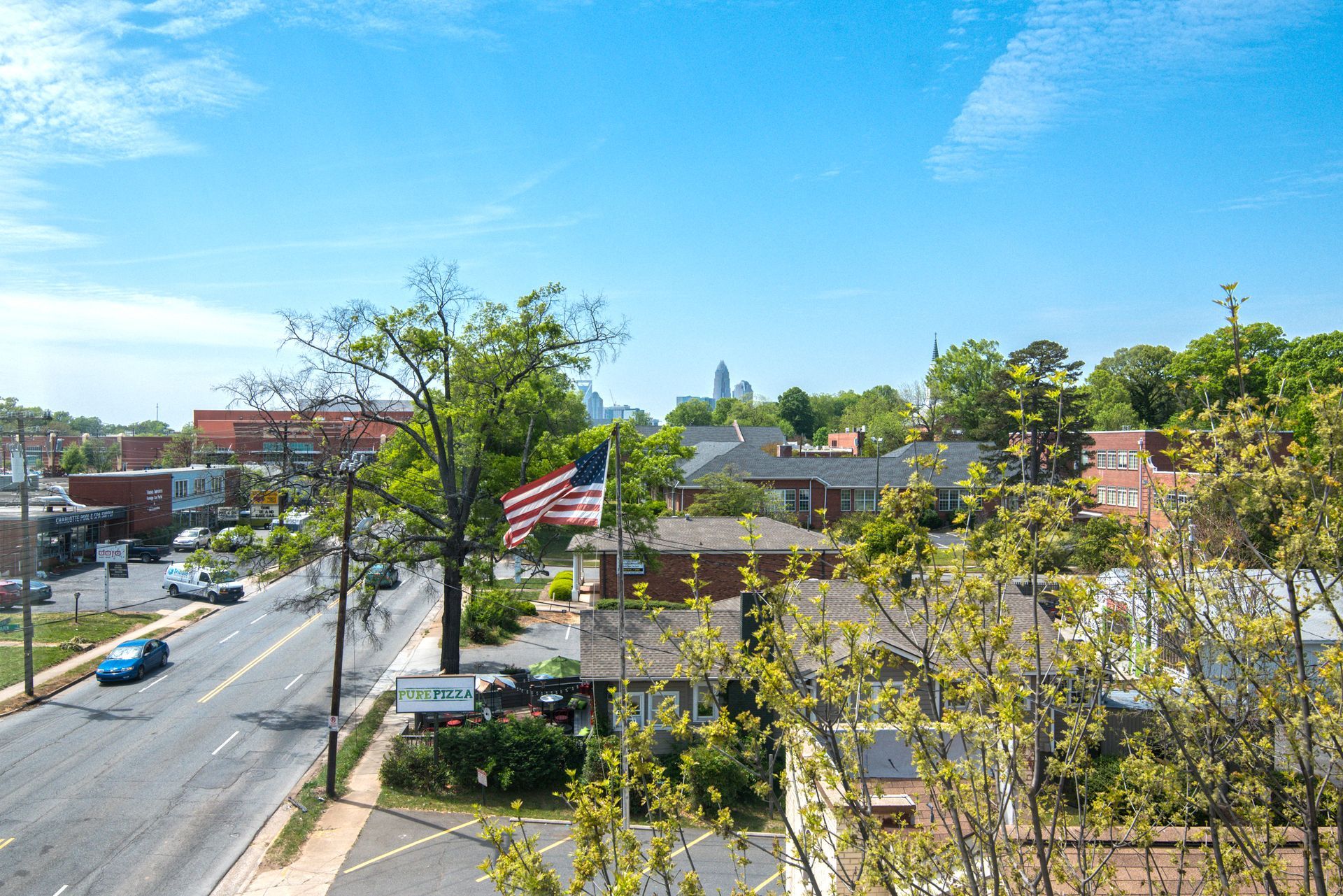 City street view with cars, businesses, and the American flag under a blue sky at Marvel Apartments.