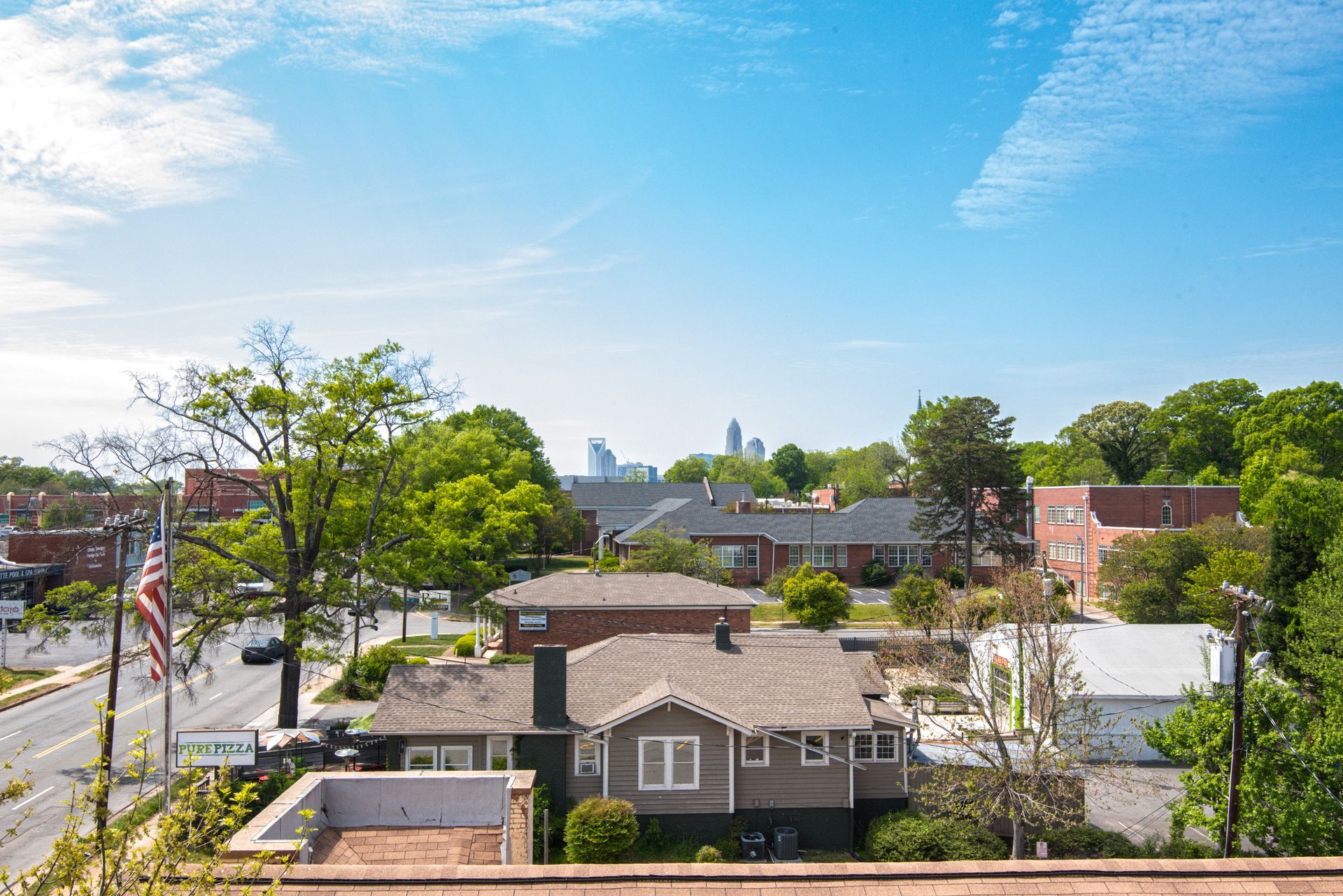 Suburban neighborhood with houses, trees, American flag, and a distant city skyline under a blue sky at Marvel Apartments.