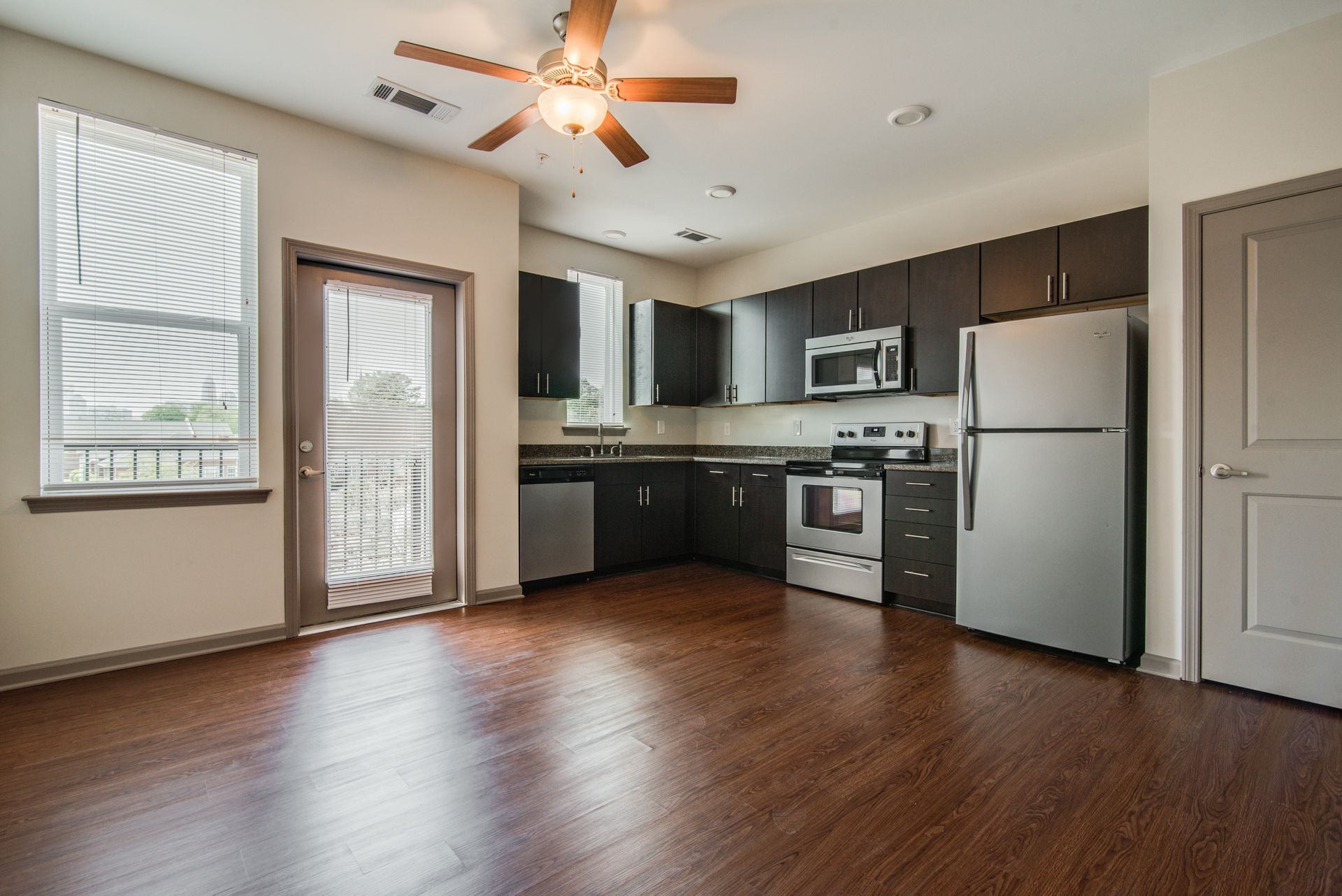 Empty kitchen with dark cabinets, stainless steel appliances, and hardwood floors at Marvel Apartments.