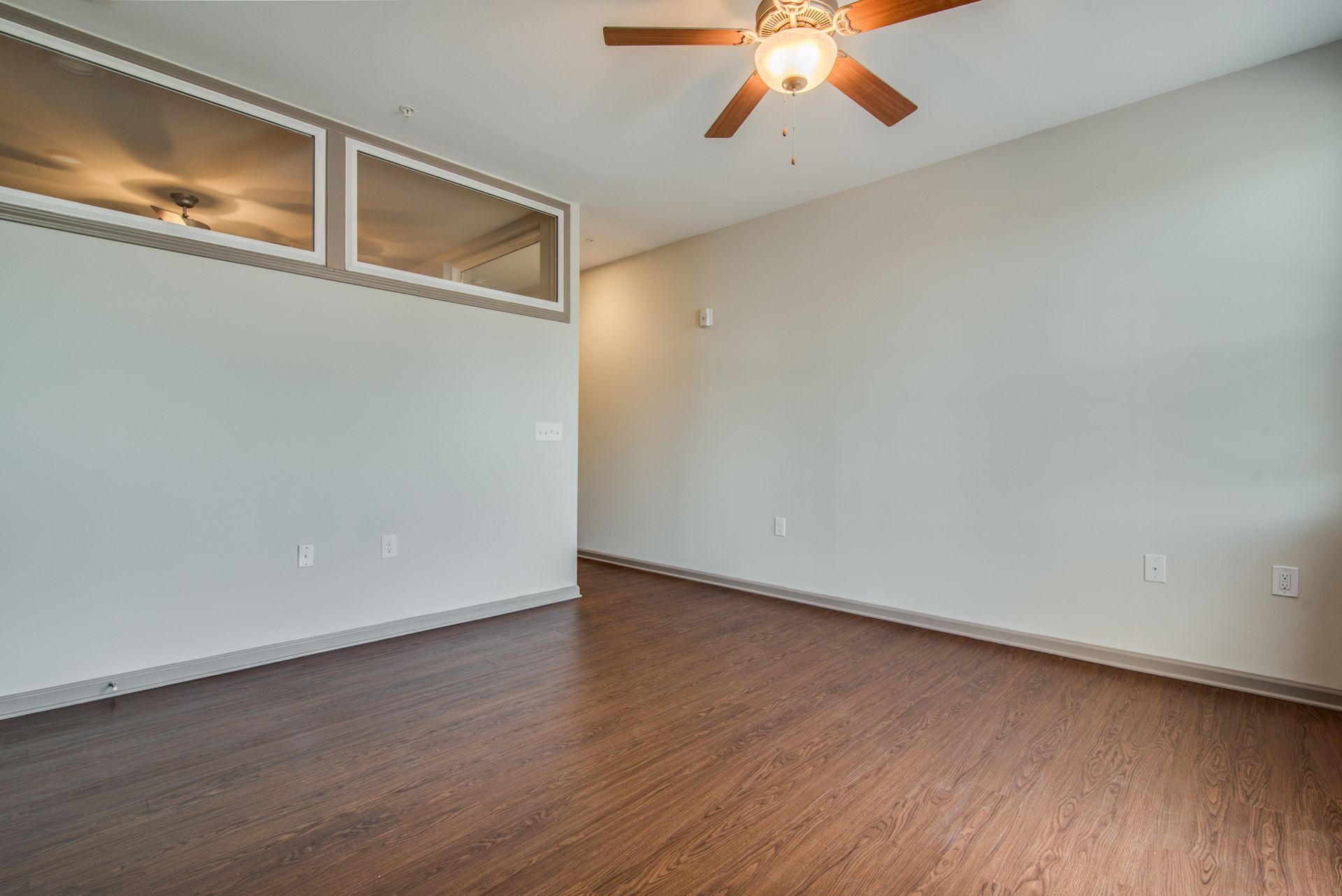 Empty room with wood flooring, pale walls, and a ceiling fan at Marvel Apartments.