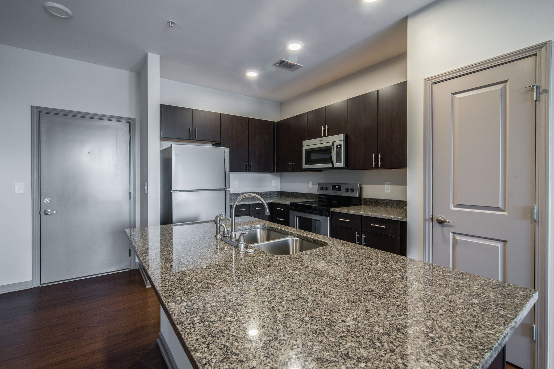 Kitchen with granite countertops, dark cabinets, stainless steel appliances, and a wooden floor at Marvel Apartments.