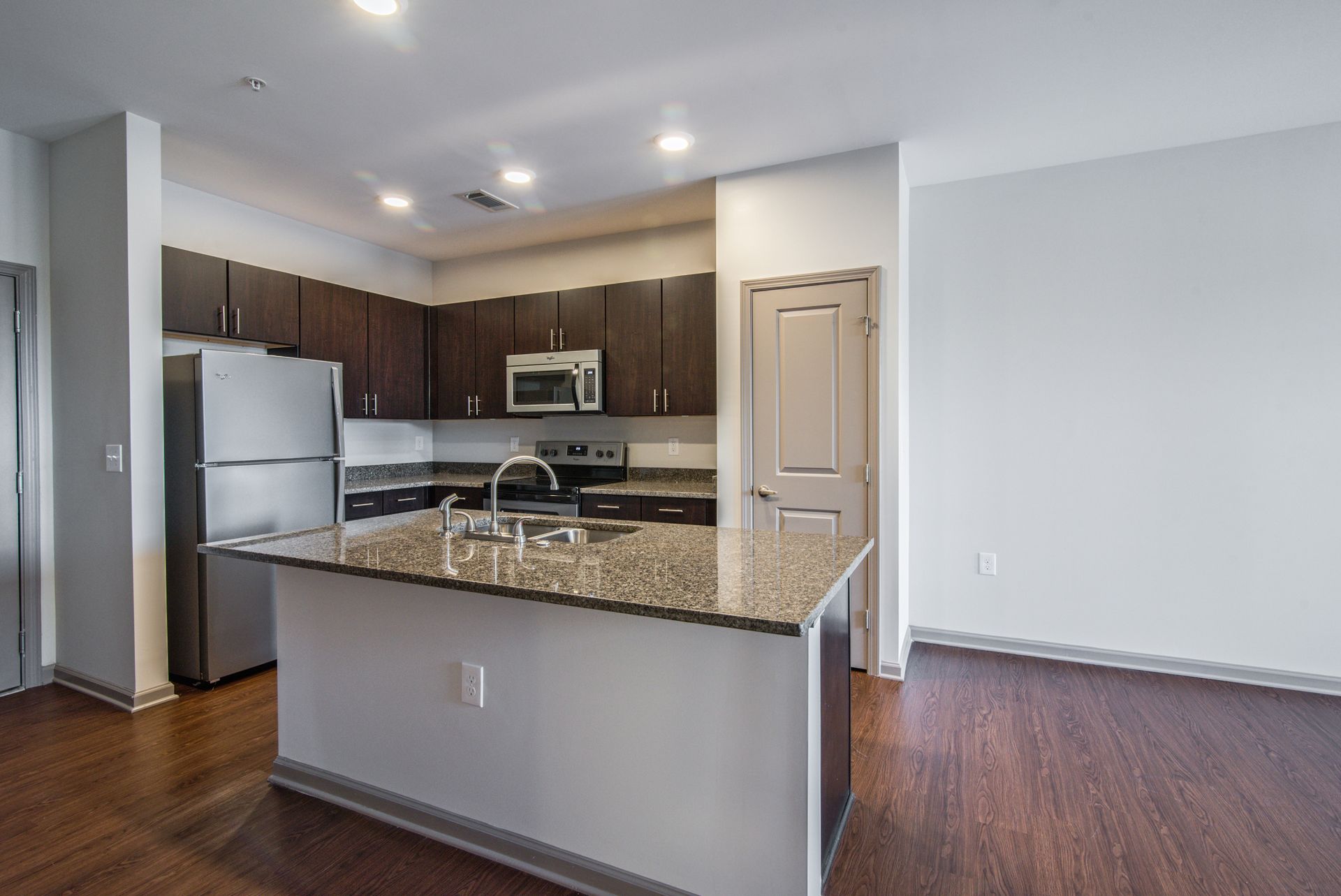 Modern kitchen with dark wood cabinets, stainless steel appliances, granite island, and hardwood floors at Marvel Apartments.