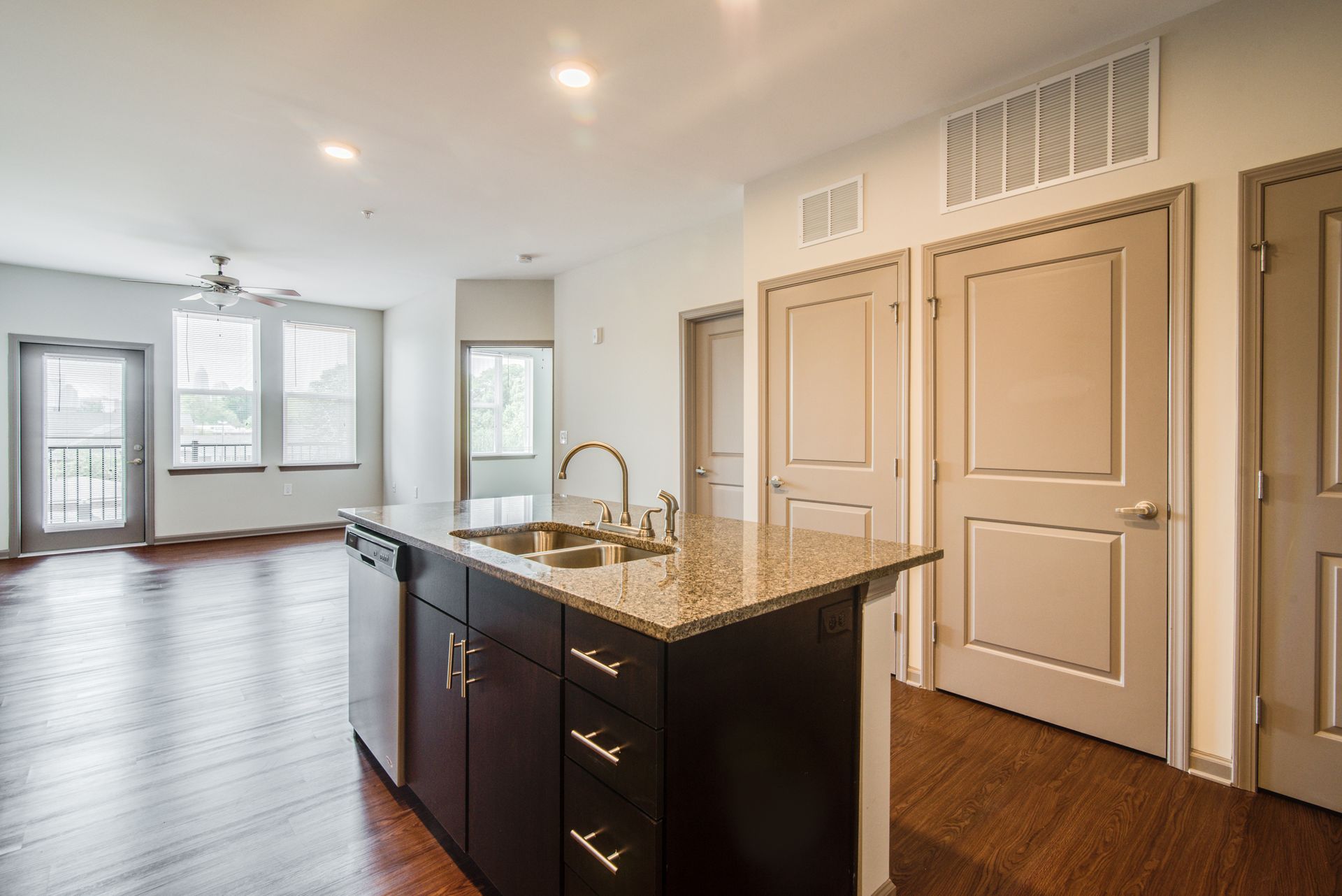 Open-concept kitchen and living room with hardwood floors, granite island, and doors to a balcony at Marvel Apartments.