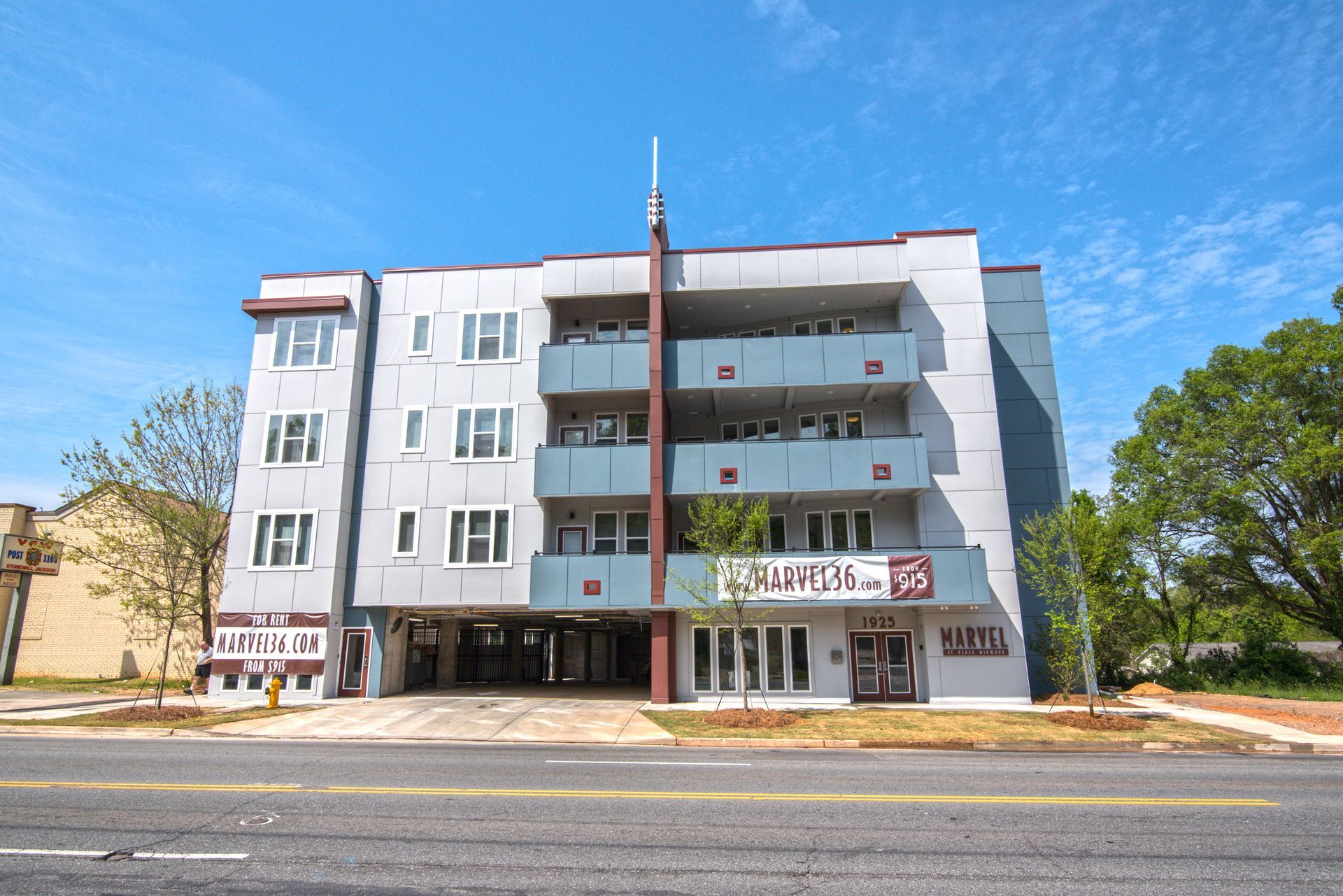 Multi-story apartment building with gray and maroon facade, built over open parking on a sunny day at Marvel Apartments.