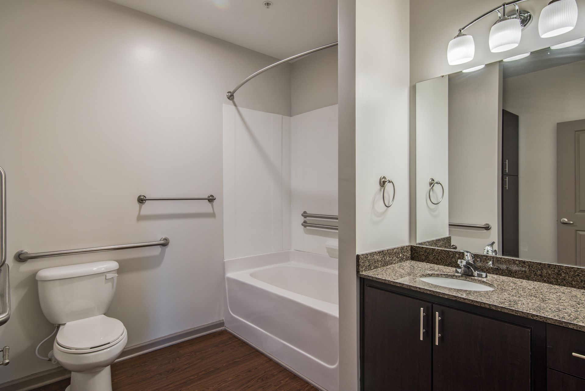 Bathroom with accessible features: toilet, tub/shower, grab bars, dark vanity with light granite countertop,and mirror  at Marvel Apartments.
