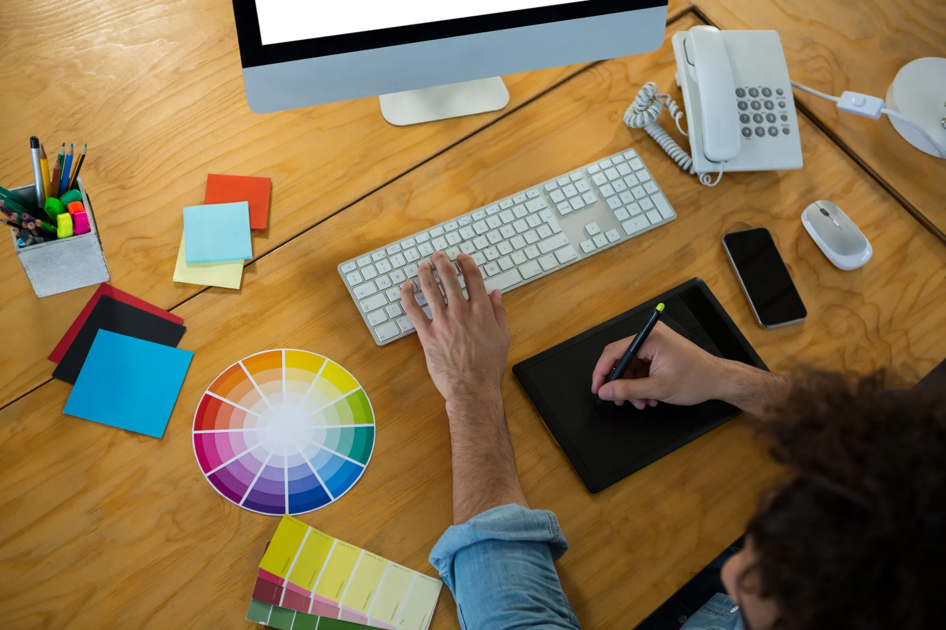 Found Here Media designer comparing color samples at a desktop keyboard for a Tucson web design project.