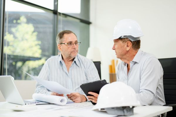 Two people in hard hats review blueprints at a construction table in a bright office