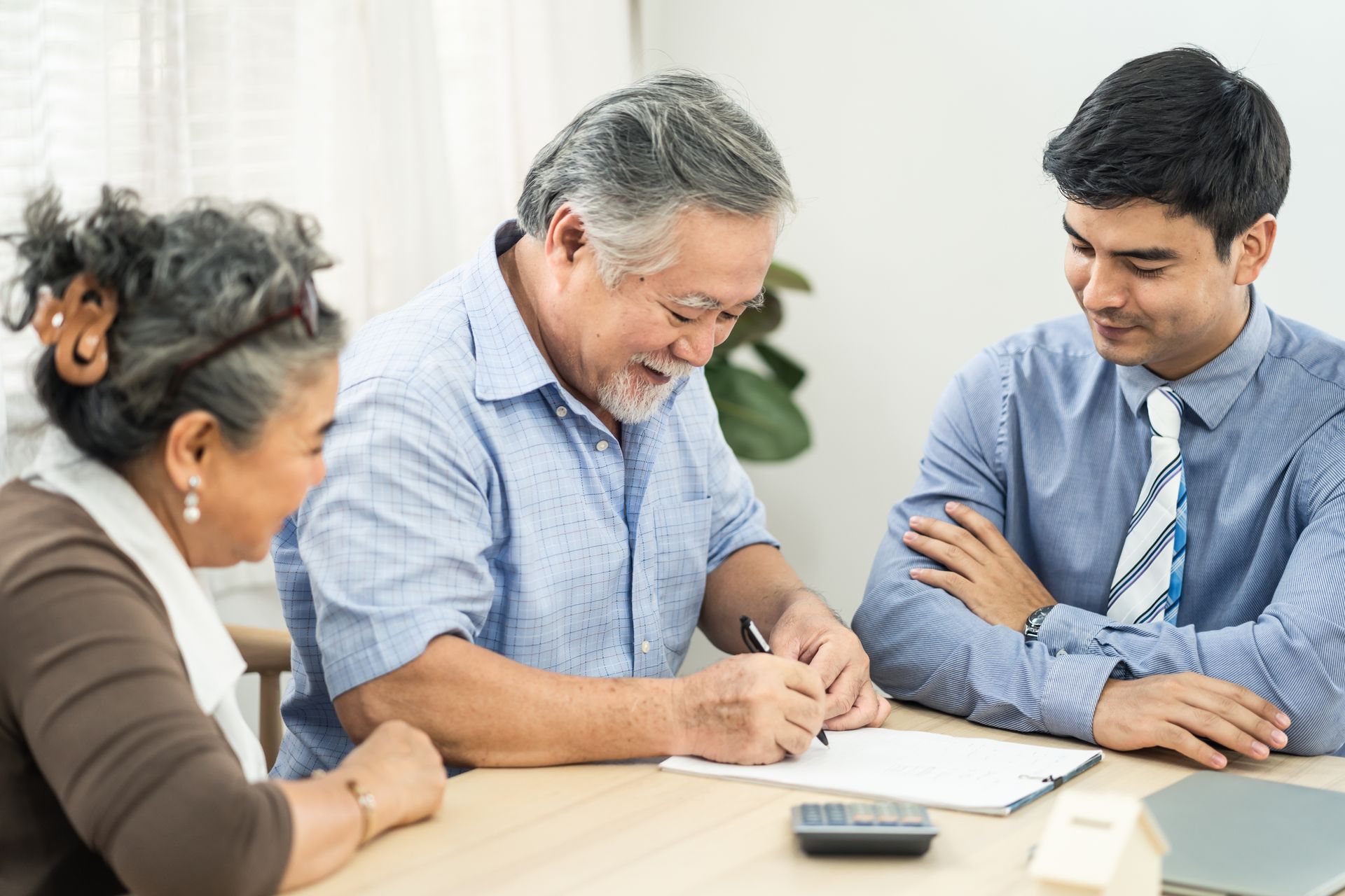 Three people reviewing documents at a table, with one writing and a calculator in the foreground.