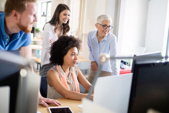 Coworkers collaborating around a desktop computer in a bright office.