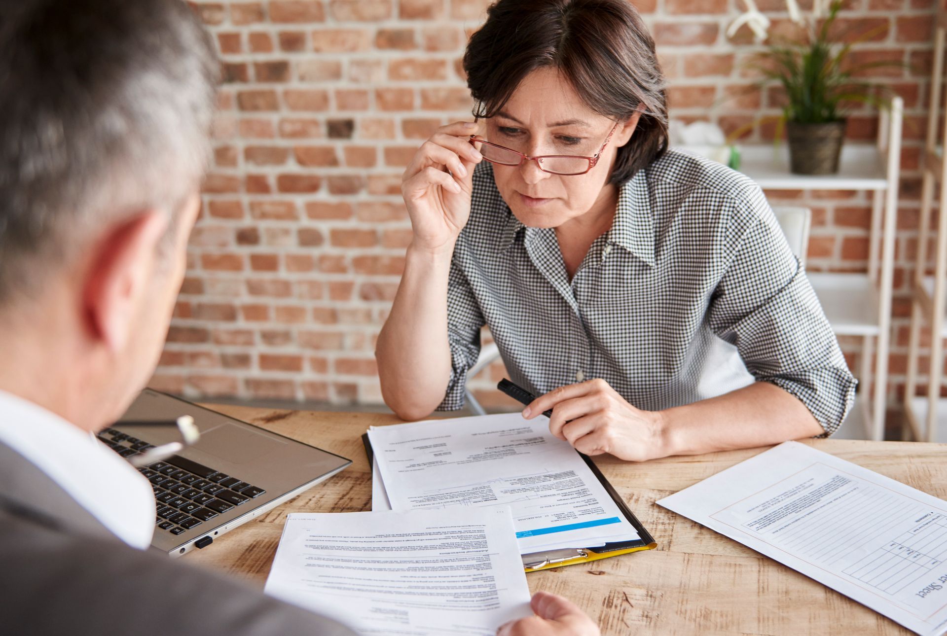 Two people reviewing paperwork at a desk in a brick-walled office