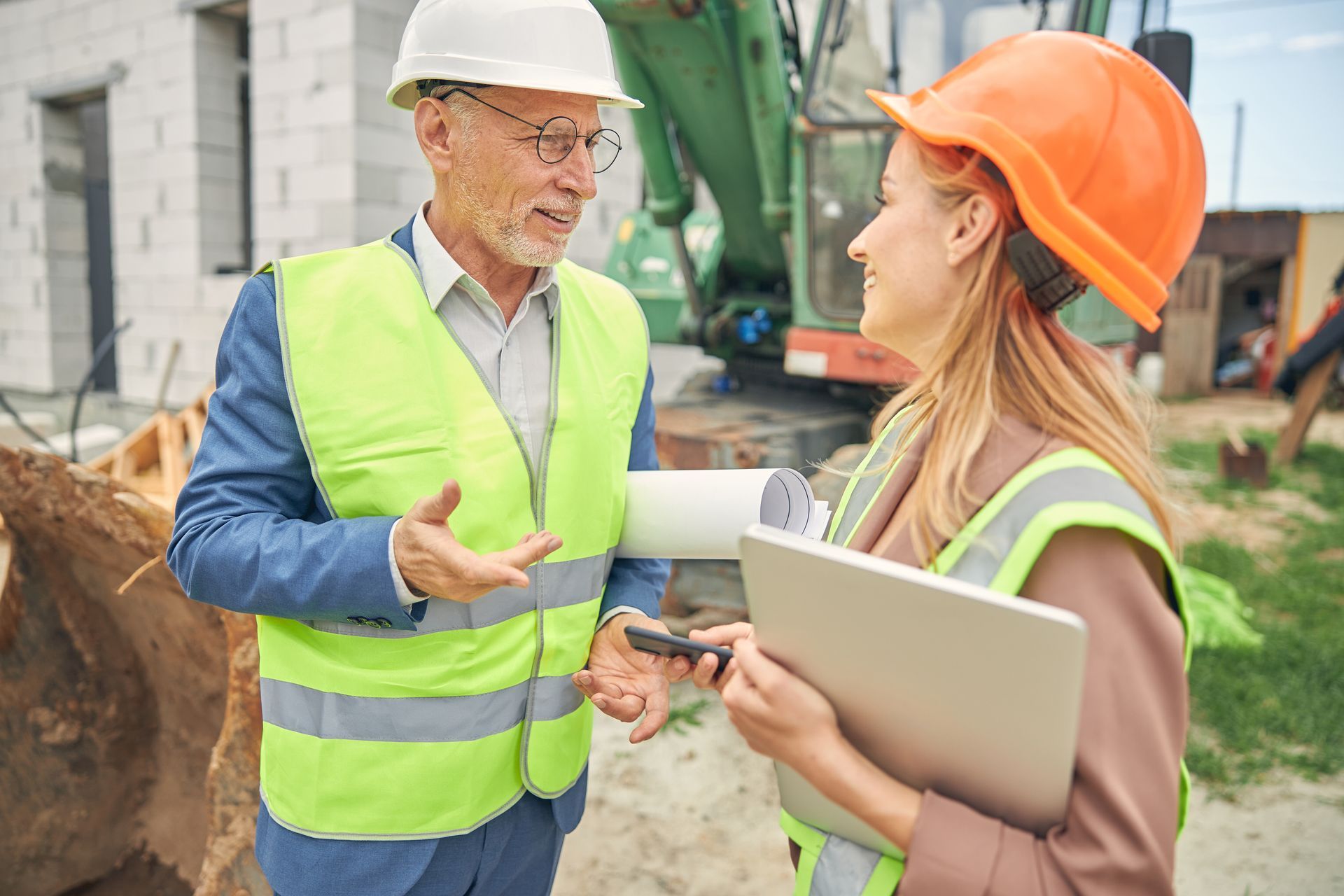 Two construction workers in hard hats and safety vests talking at a work site