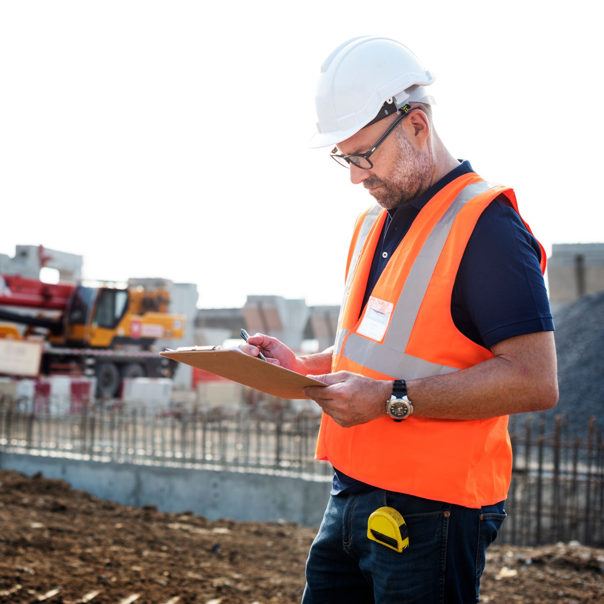 Construction worker in orange safety vest and hard hat reviewing plans on a clipboard at a worksite