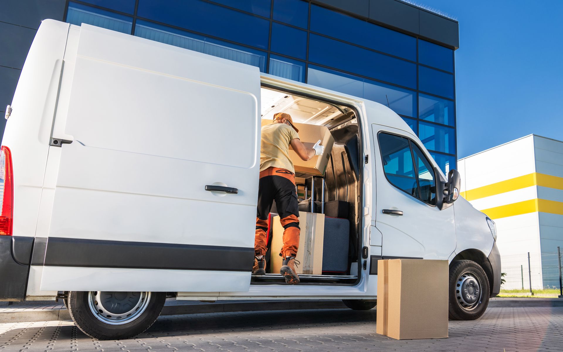 White delivery van with open side door outside a building, boxes beside it