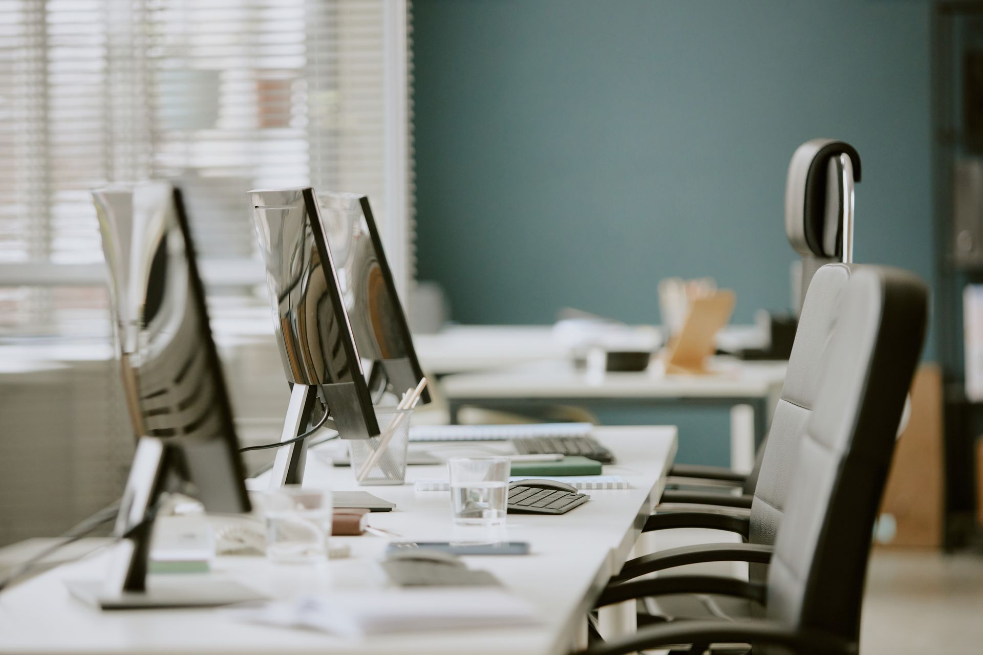 Modern office with rows of desktop computers and empty swivel chairs on white desks