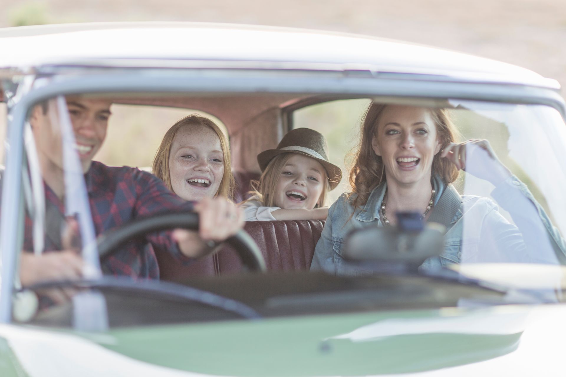 Four smiling people in a vintage car, seen through the windshield.