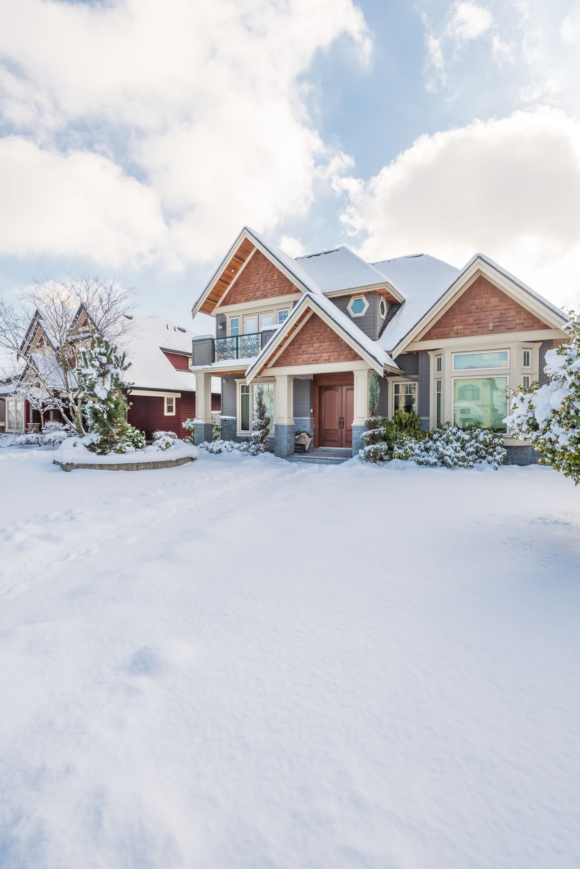 Snow-covered suburban house with a red brick entry and cloudy winter sky