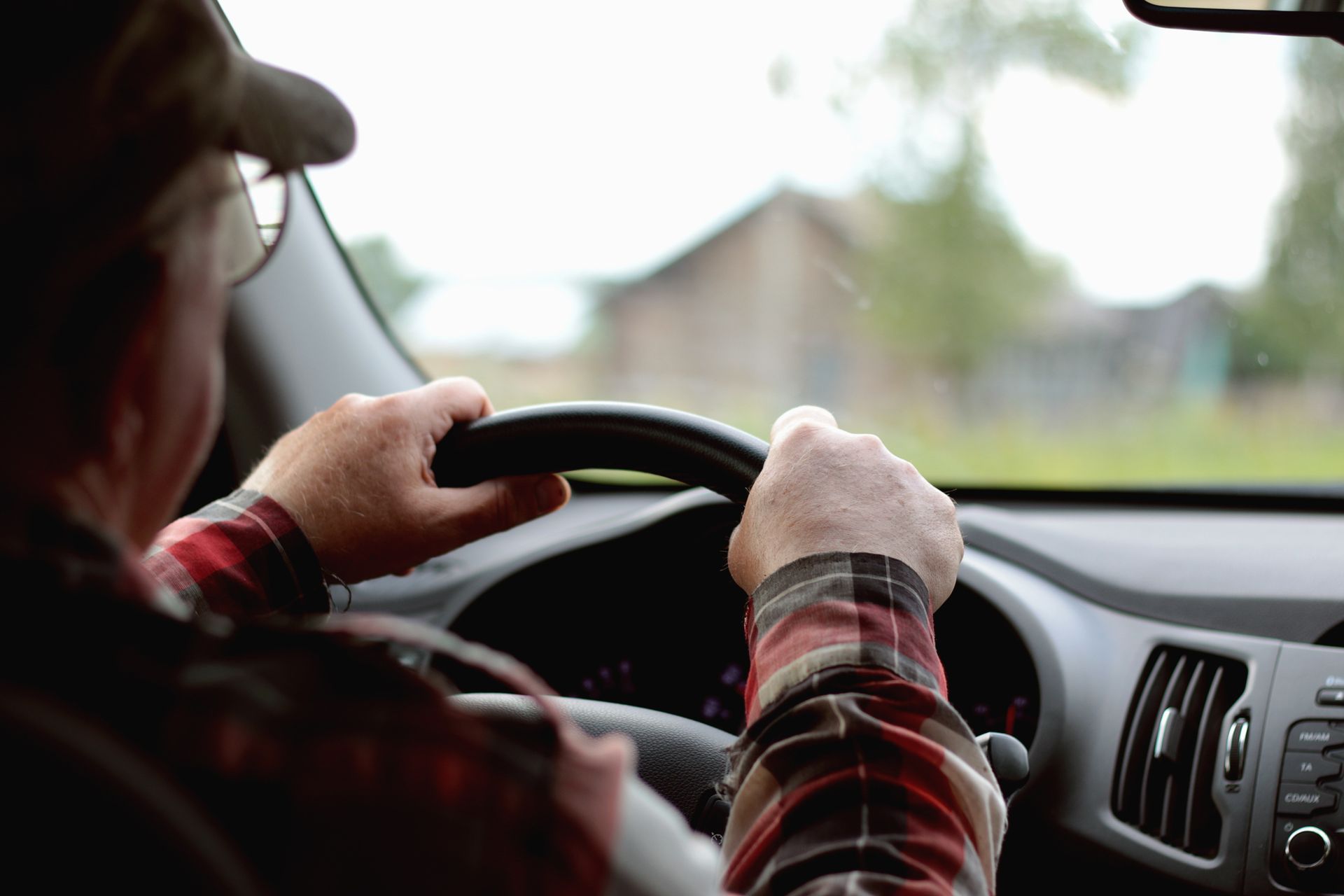 Driver holding a steering wheel inside a car, looking out at a blurred rural road.