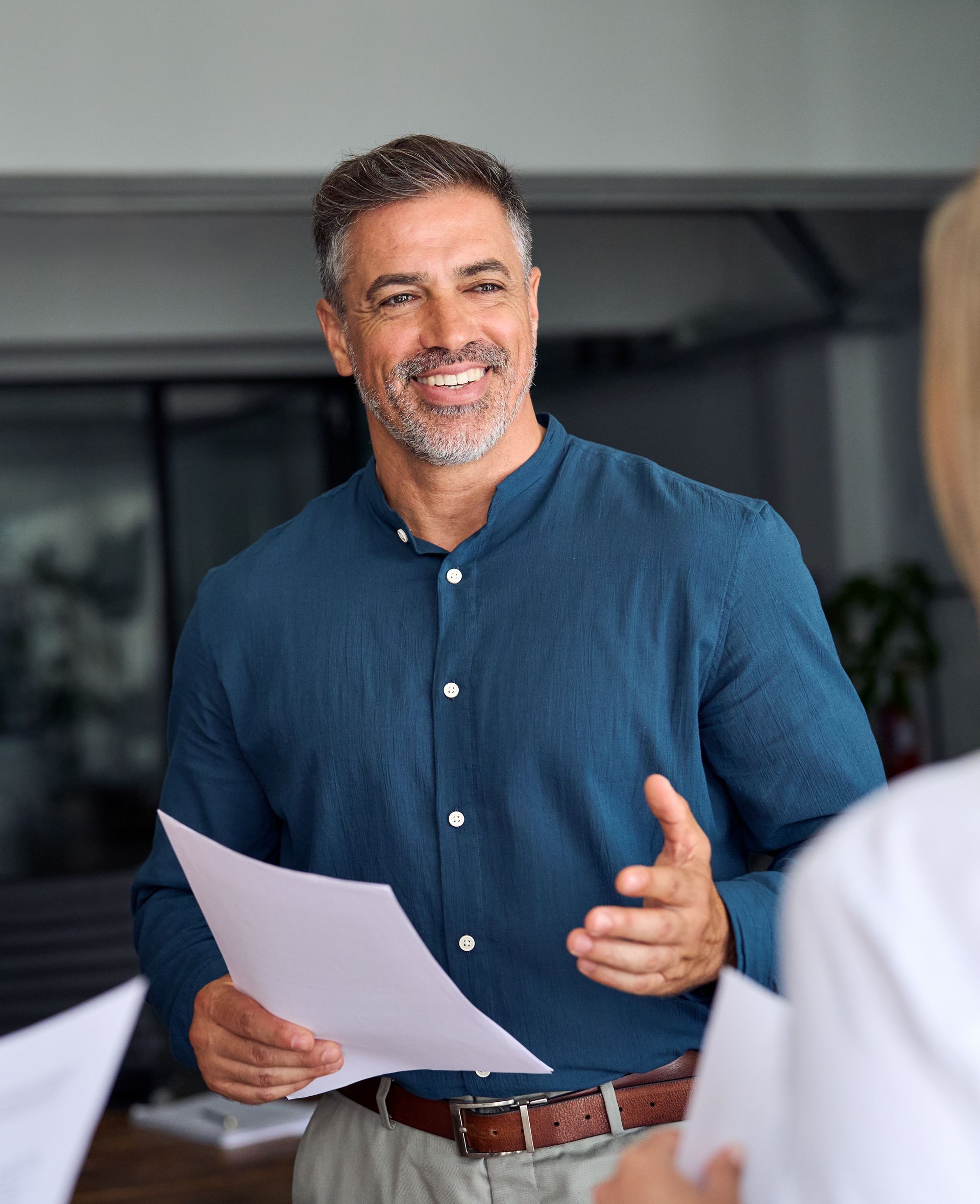 Smiling man in blue shirt holding papers and speaking in a meeting room