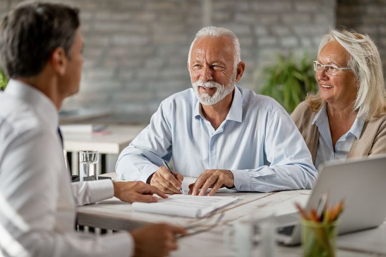 Three people discuss documents at a table in a bright office meeting room.
