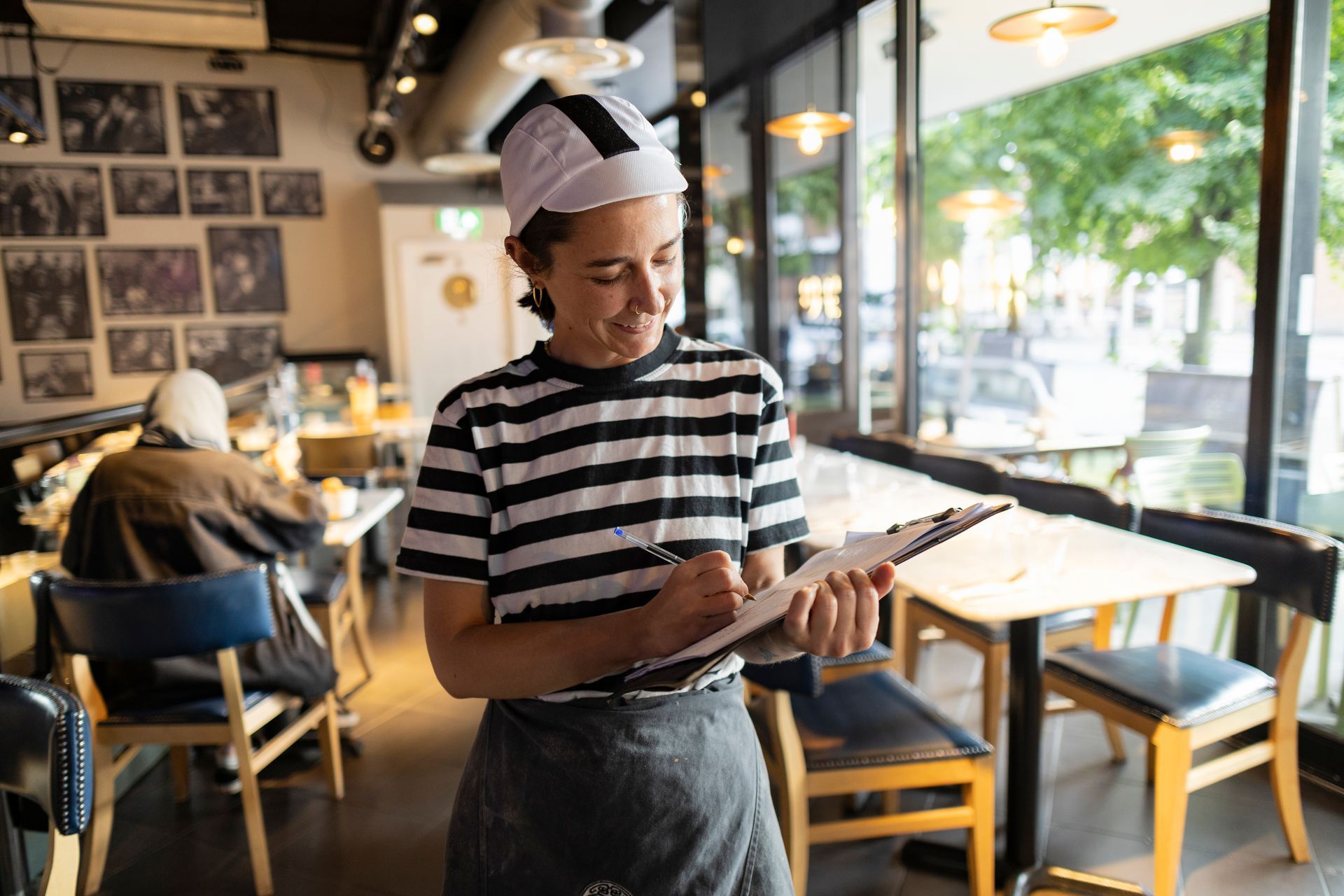 Cafe worker taking notes beside tables in a bright, modern restaurant