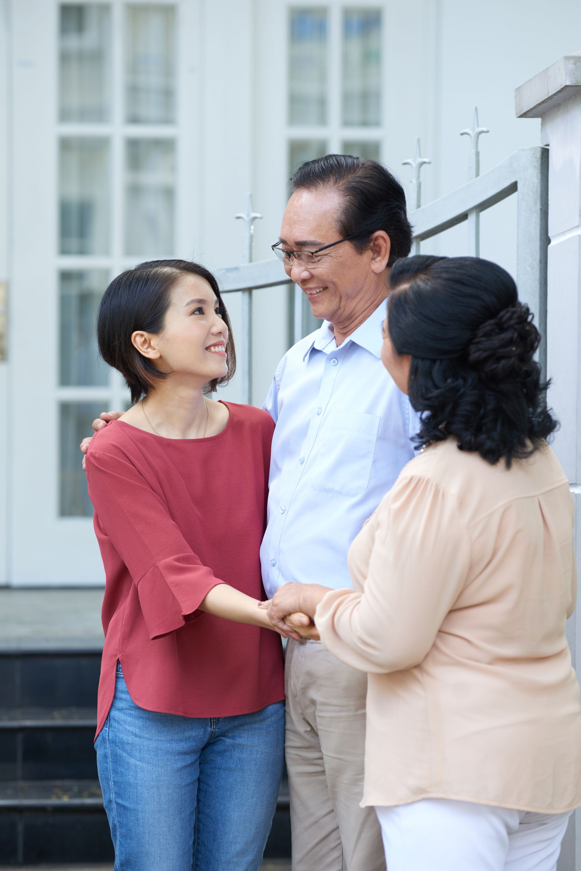 Three people smiling and holding hands outside a building entrance