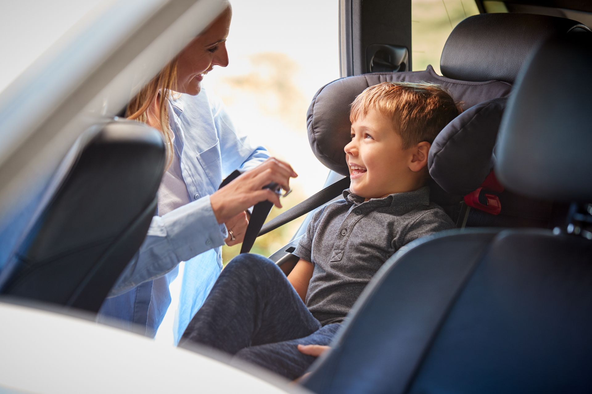 Adult handing a smiling child a snack in a car’s back seat