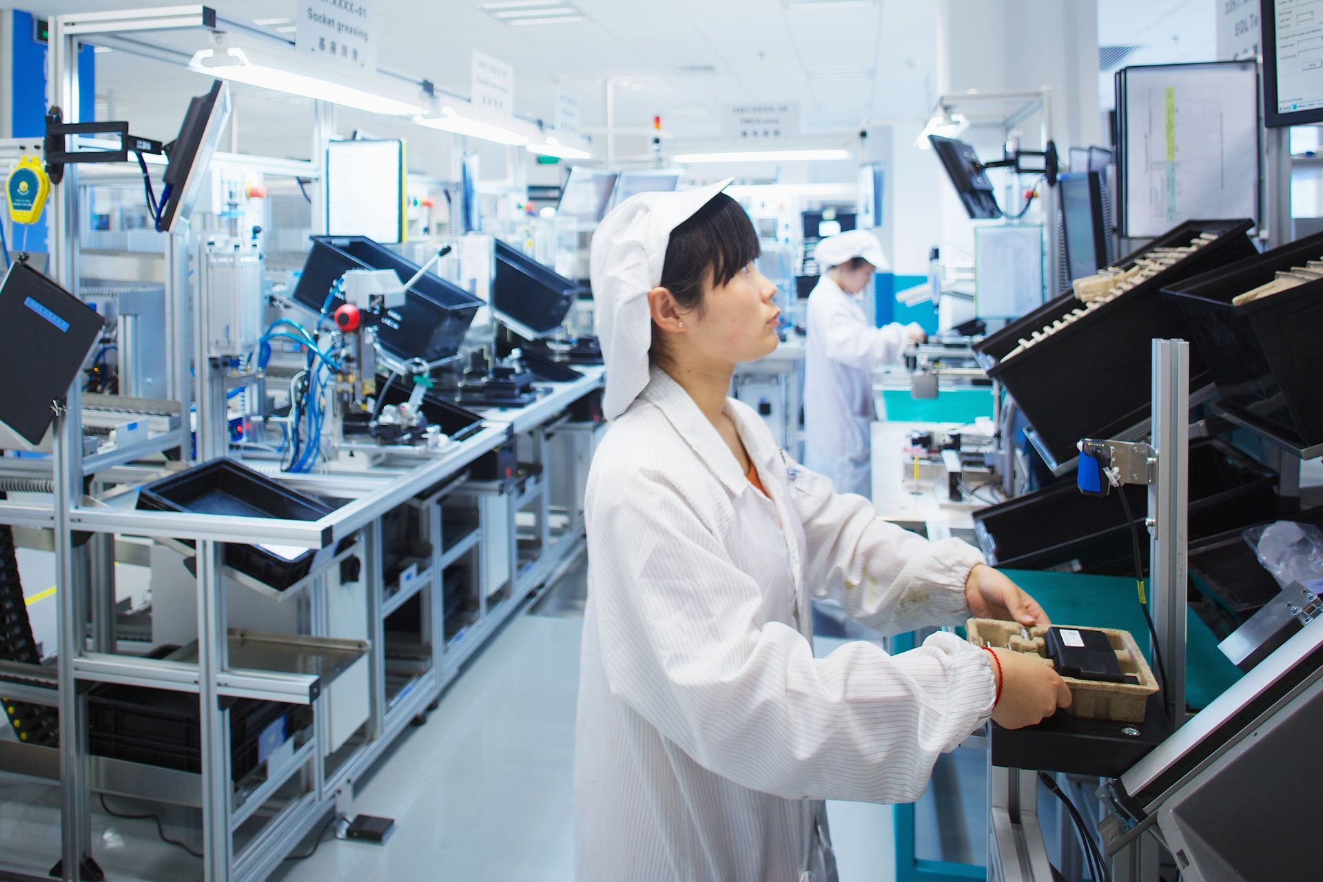 Technician in a white lab coat working at a semiconductor assembly machine in a bright factory.