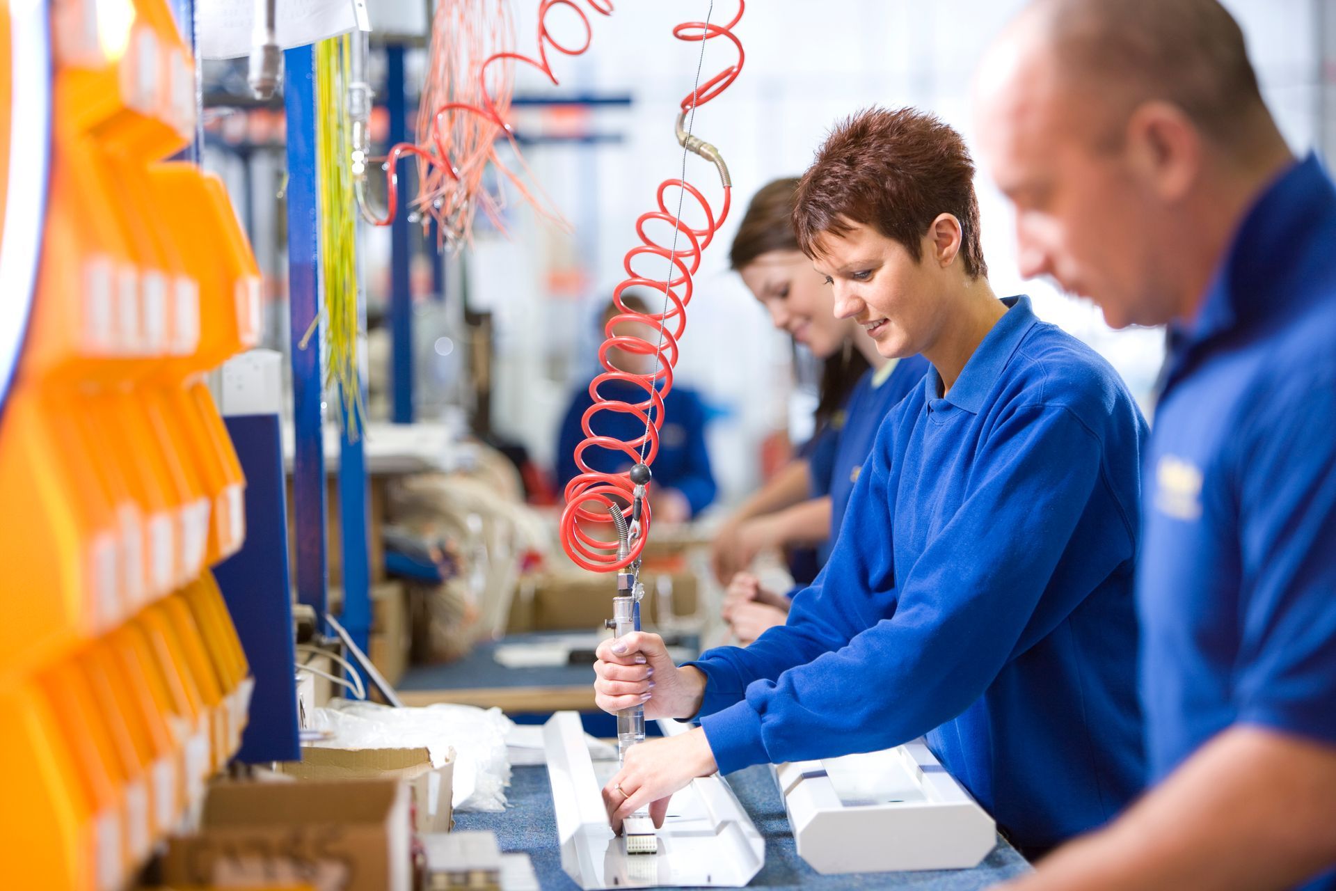 Workers in blue uniforms assembling products on a factory line with orange equipment and boxes