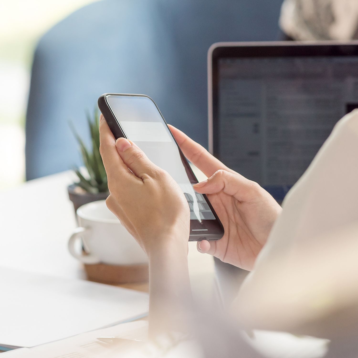 A person is using a cell phone in front of a laptop