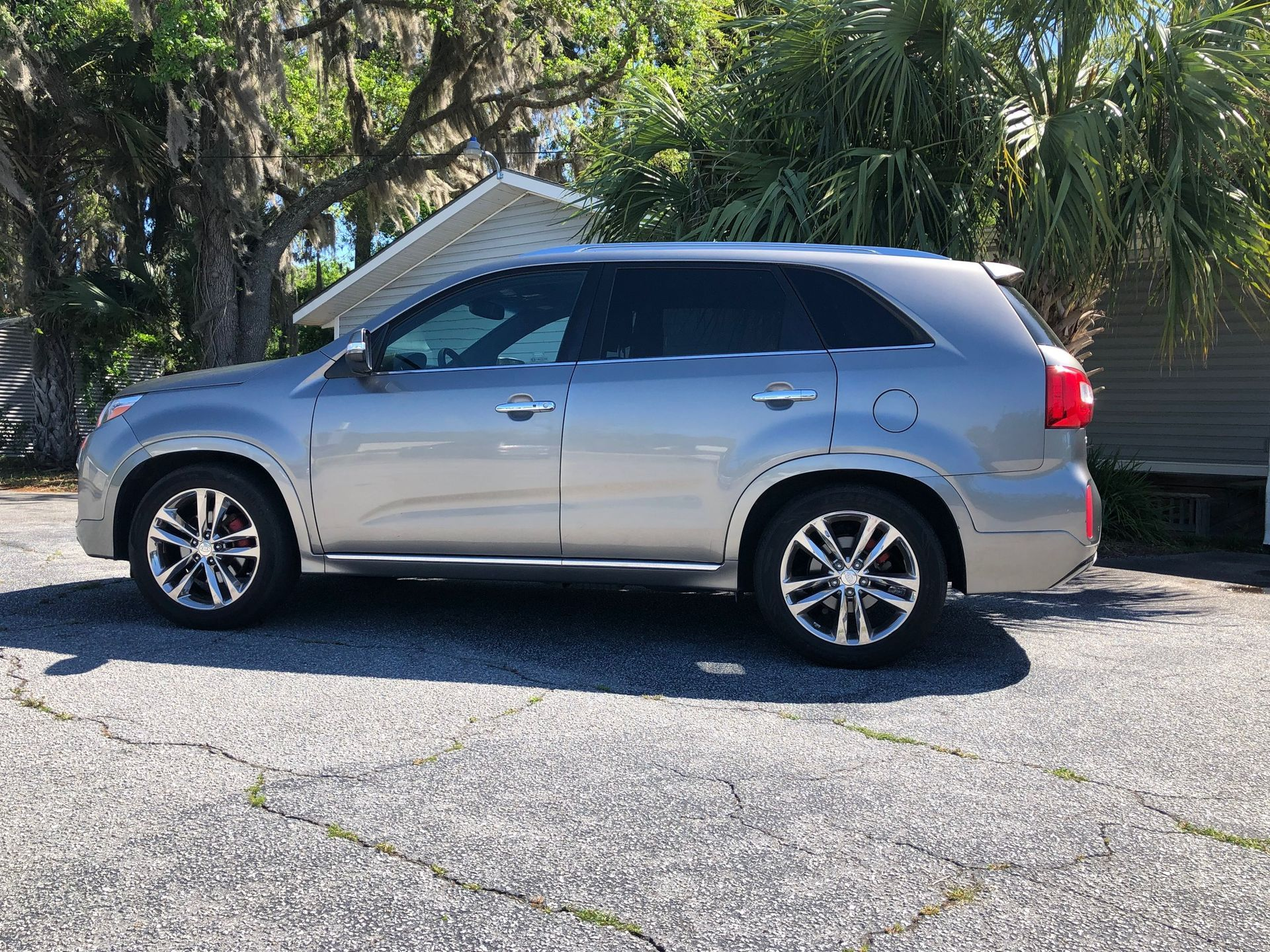 Silver SUV parked on a cracked asphalt lot with a building and foliage in the background.