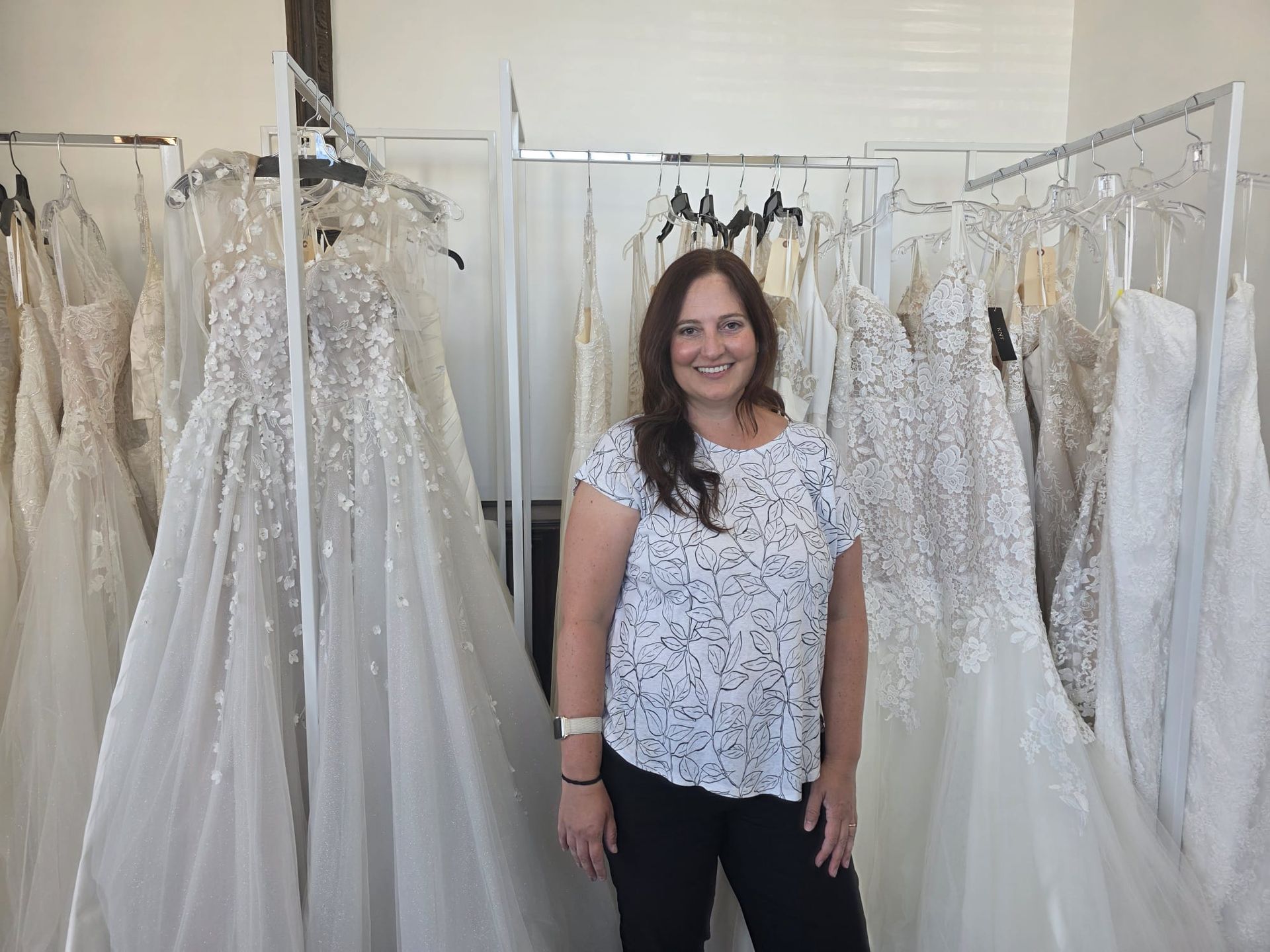 Woman smiling in a bridal shop, surrounded by wedding dresses on racks.