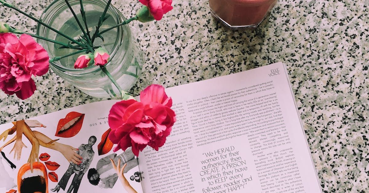 A vase of pink flowers is sitting on top of an open book on a table.
