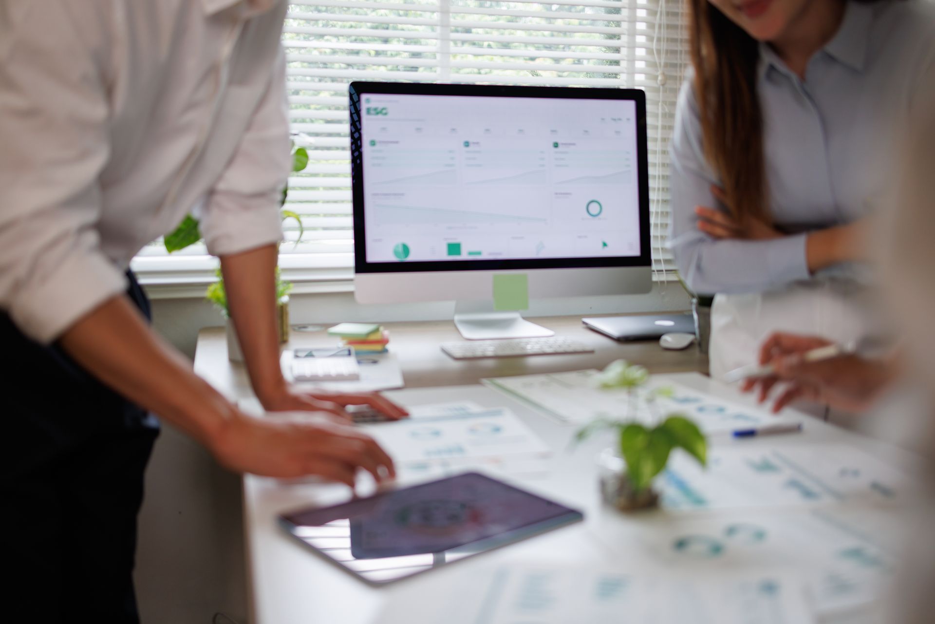Three people in a meeting reviewing documents and a tablet at a wooden table.