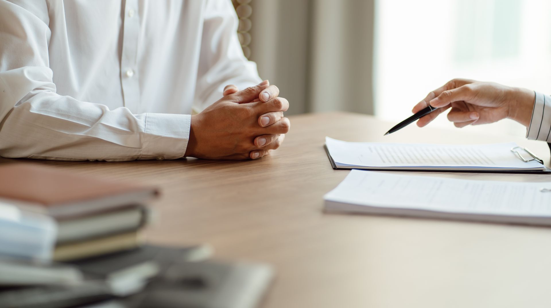 Two people at a desk in a meeting, one taking notes beside a notebook and pen.