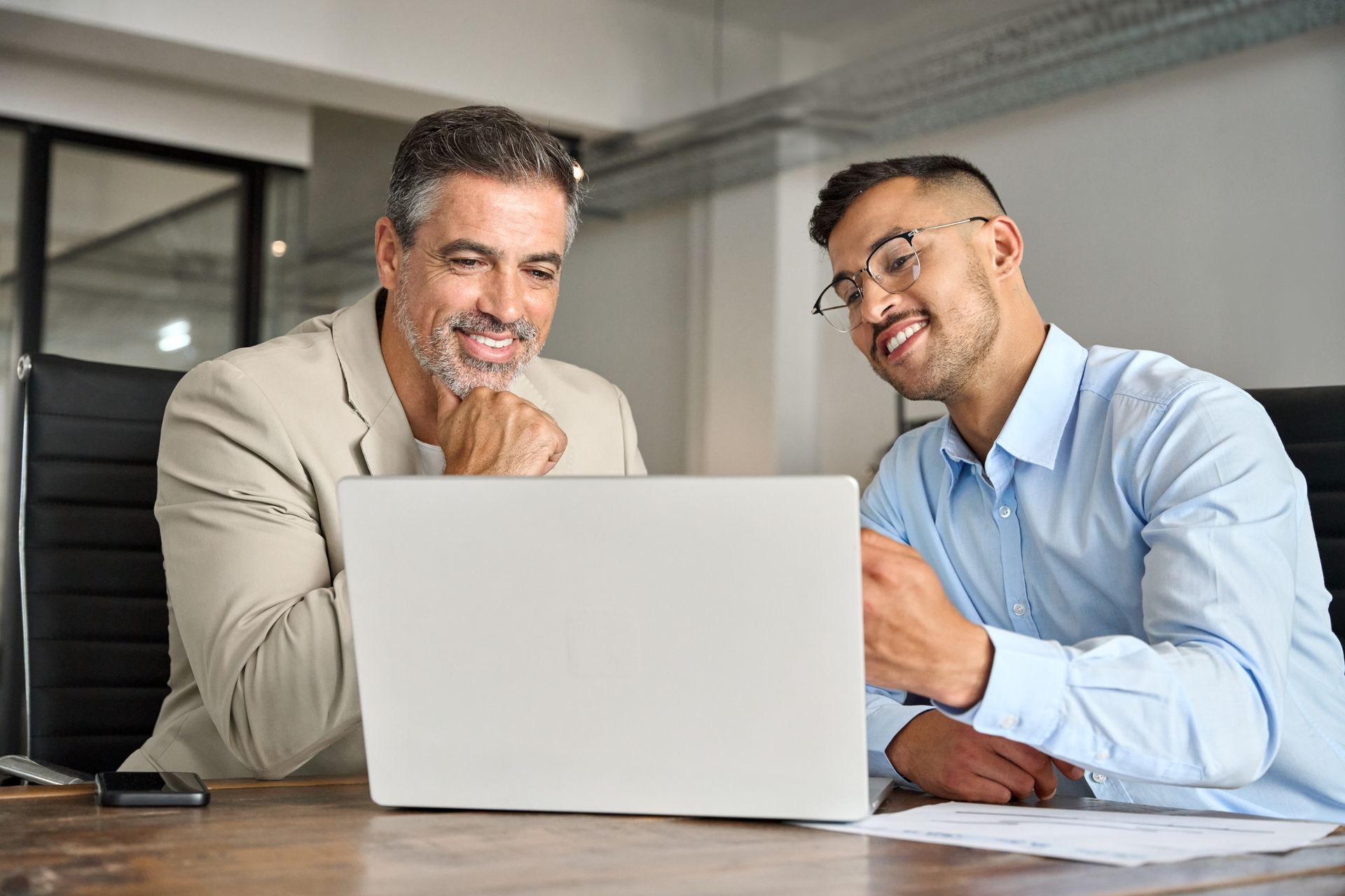 Two people smiling at a laptop in a modern office conference room