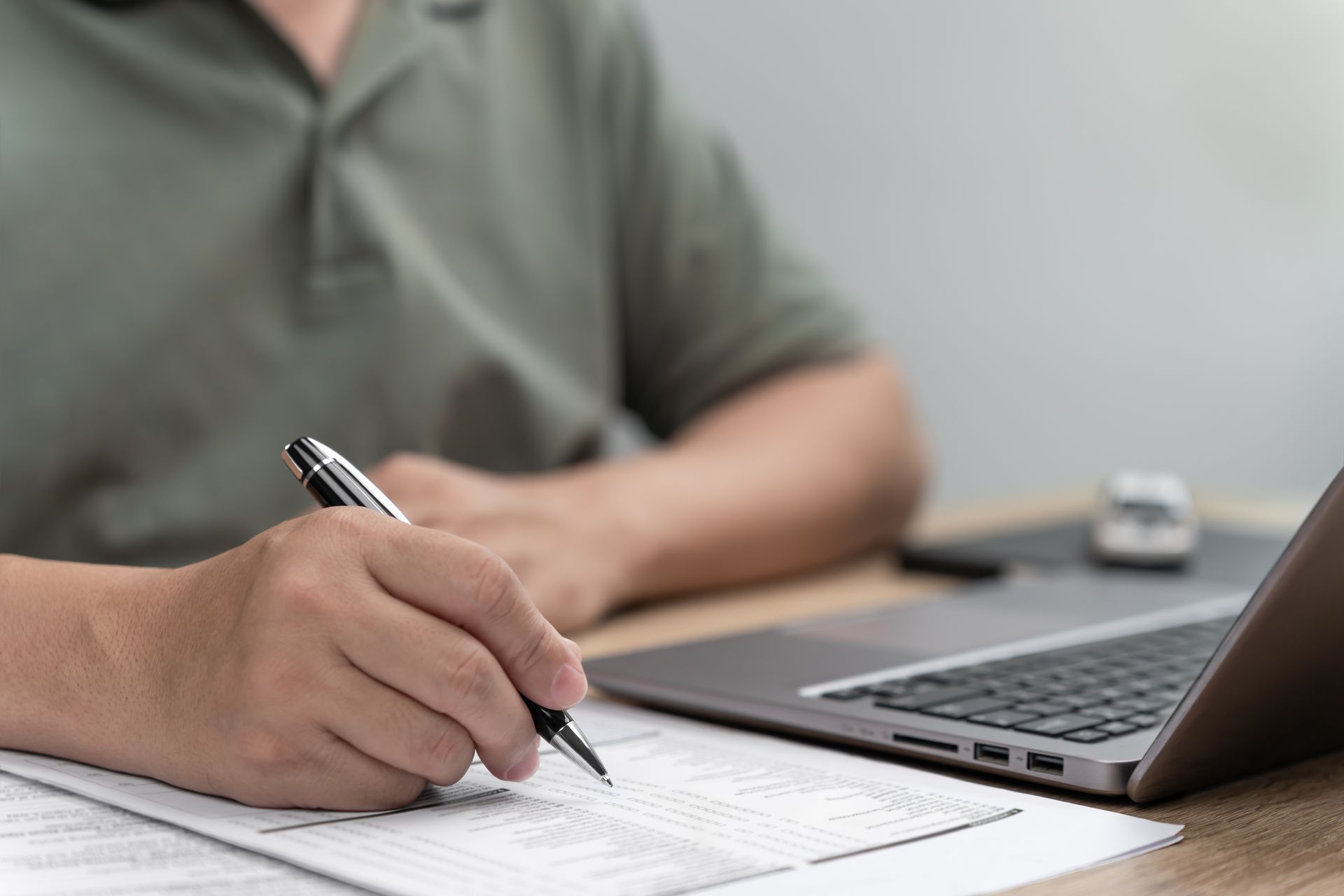 Person writing on a paper form beside a laptop on a desk