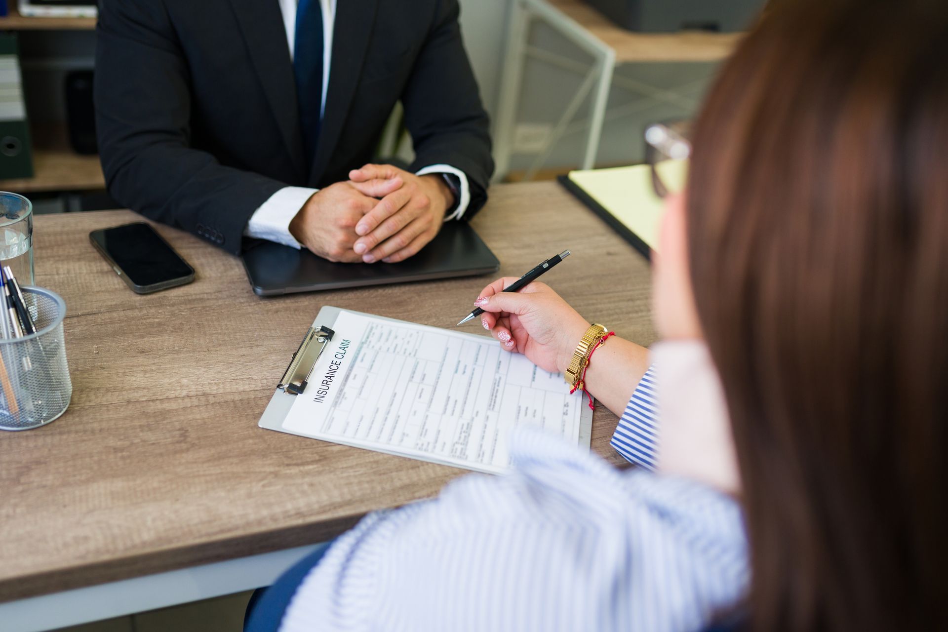 Two people in a meeting, one taking notes on a clipboard across a desk