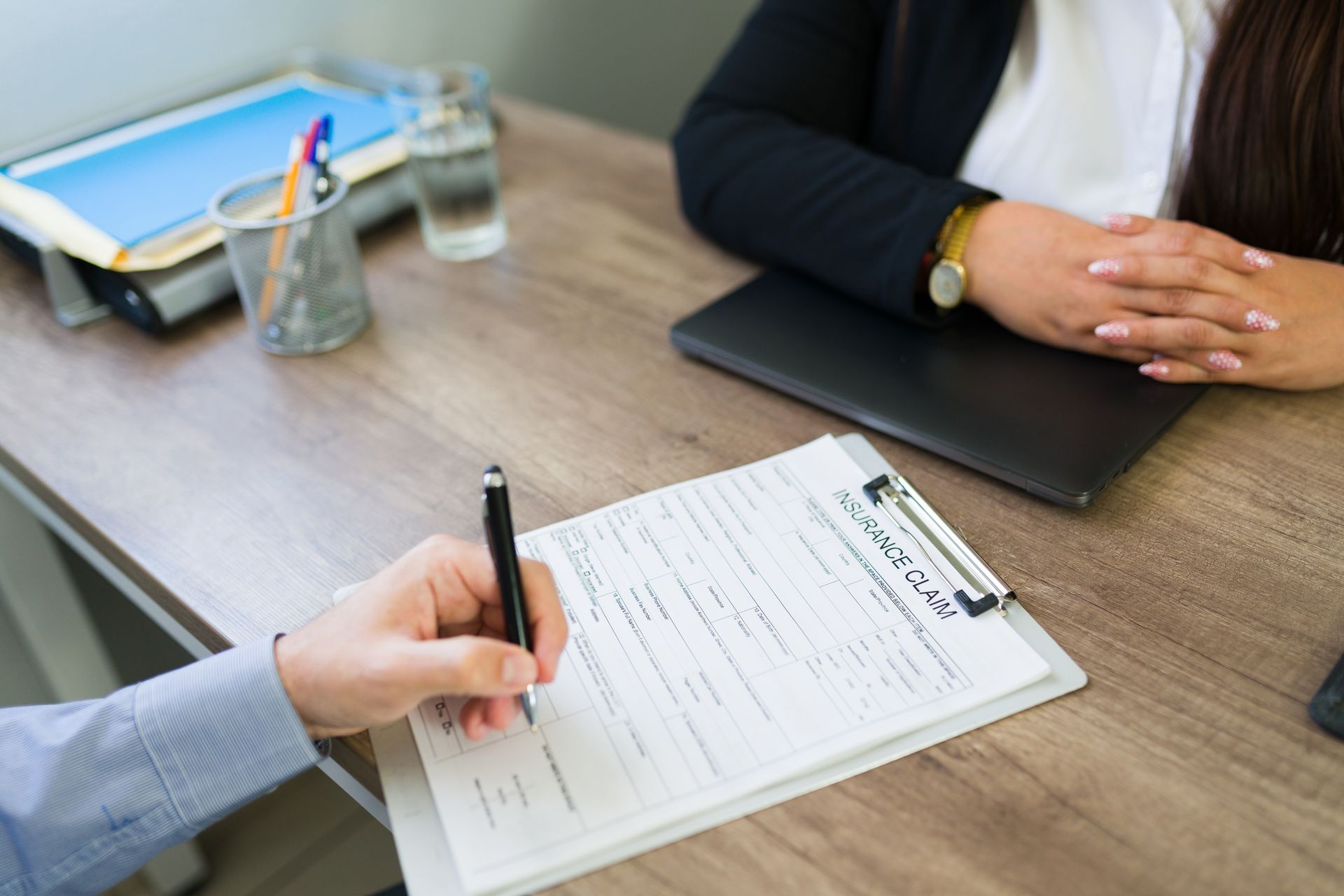 Hands signing a document across a meeting table with folders and a glass of water nearby