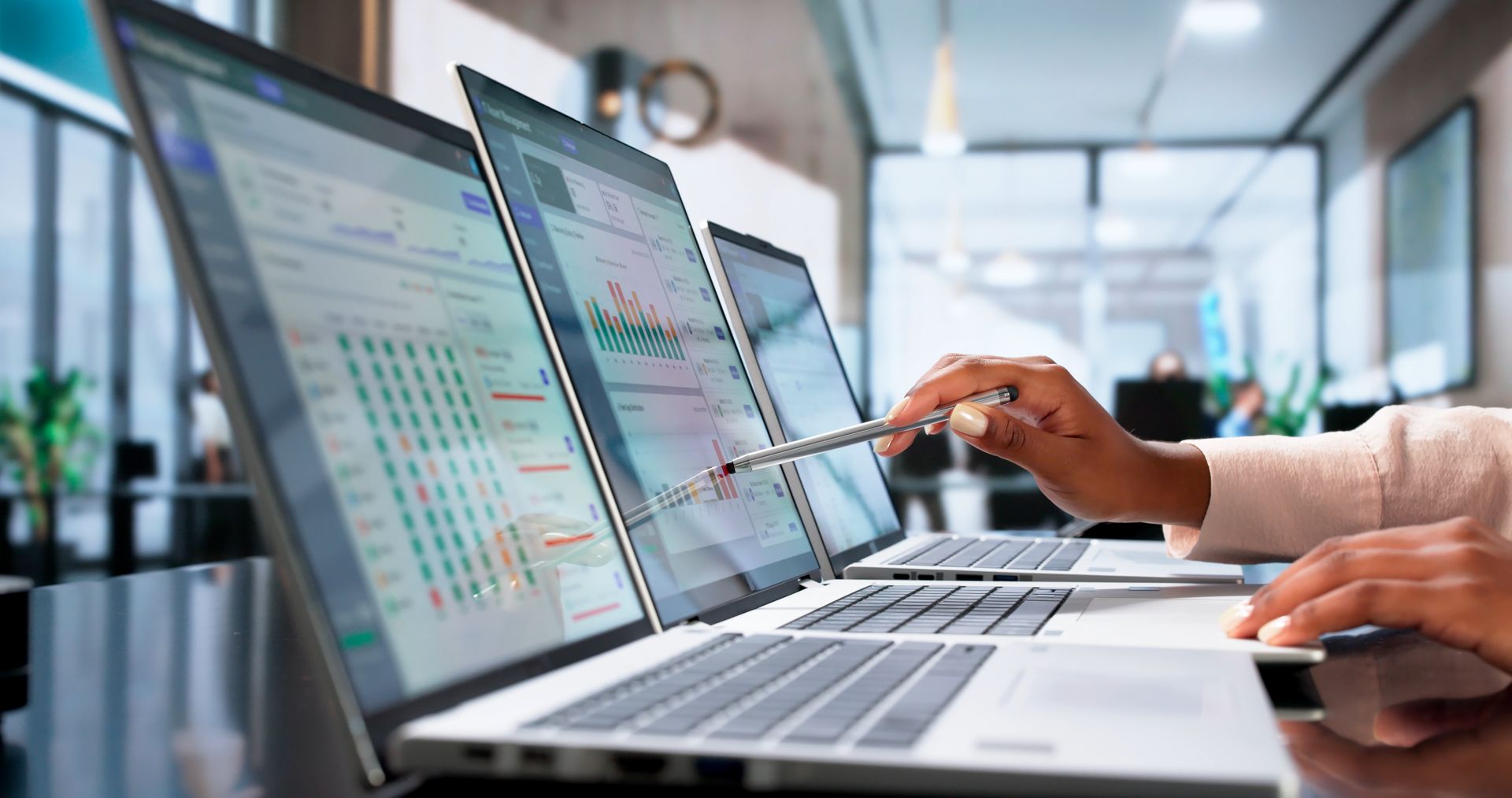 Hands pointing at laptop screens showing charts in a bright office workspace