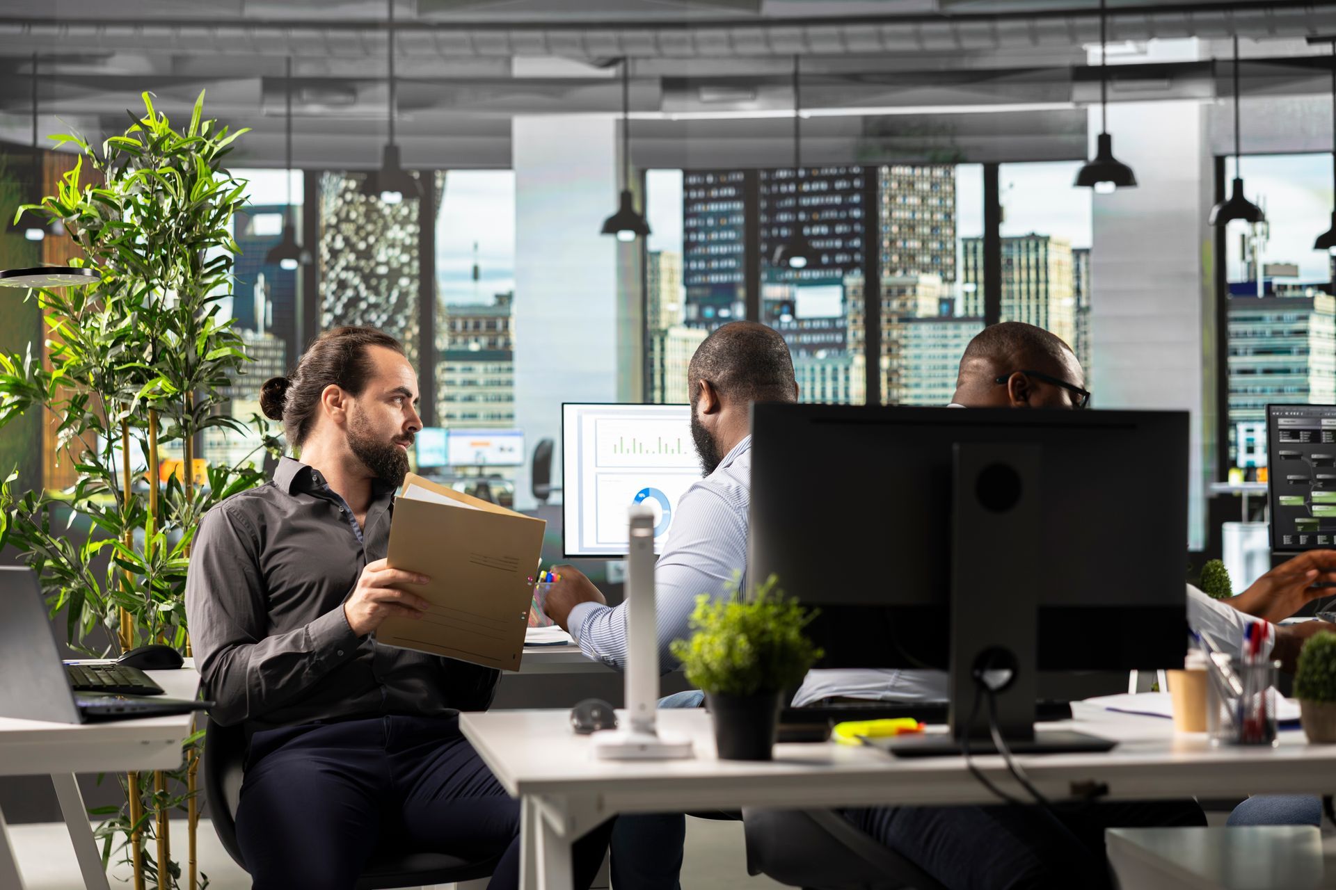 Coworkers collaborating in a bright modern office with desks, computers, and large windows