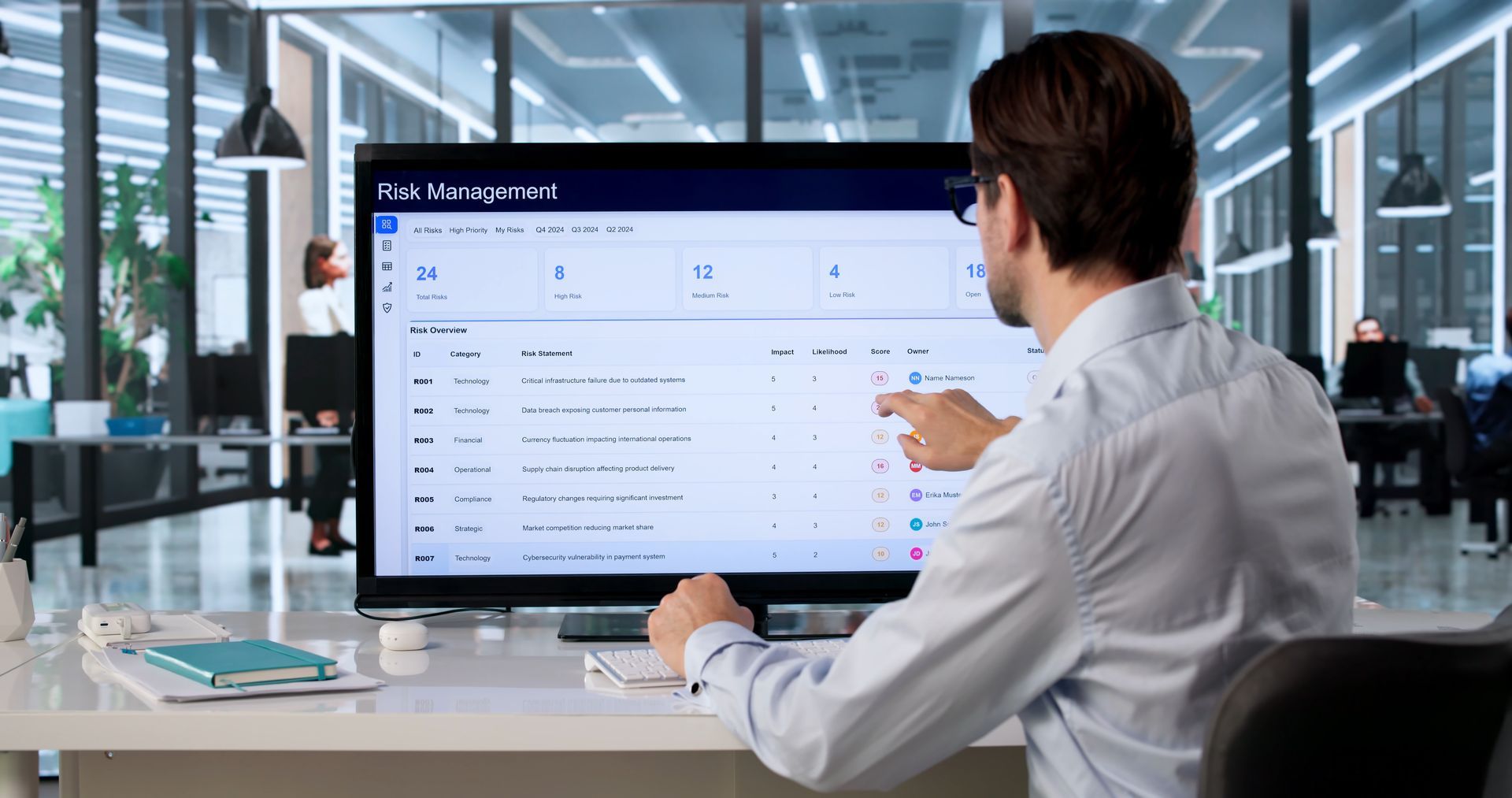 Man at desk points to a large monitor showing a task dashboard in a bright modern office