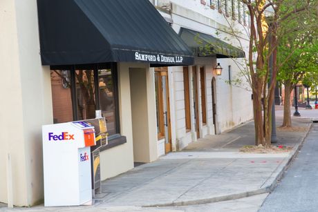 A fedex box is on the sidewalk in front of a building