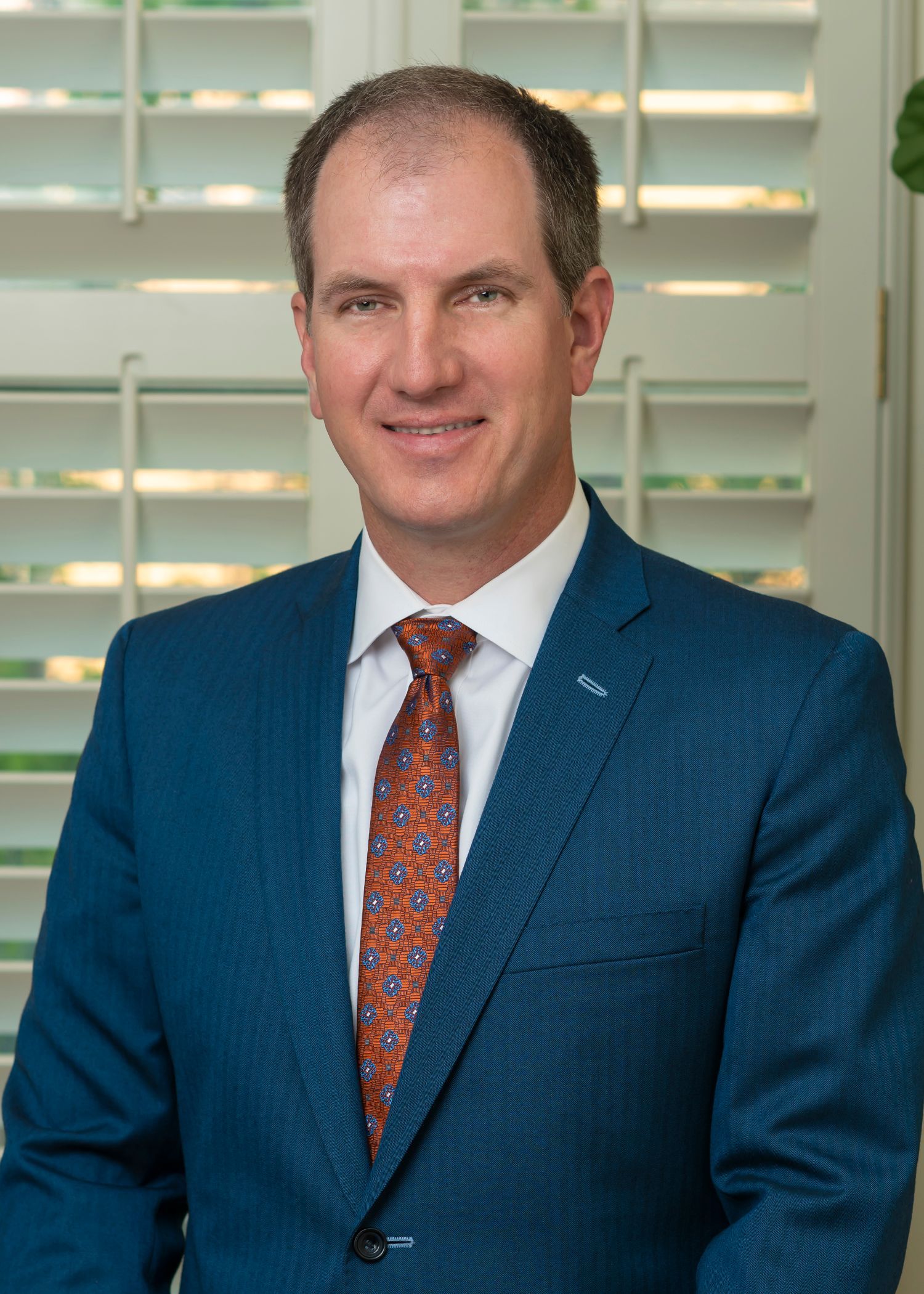 A man in a suit and tie is standing in front of shutters.