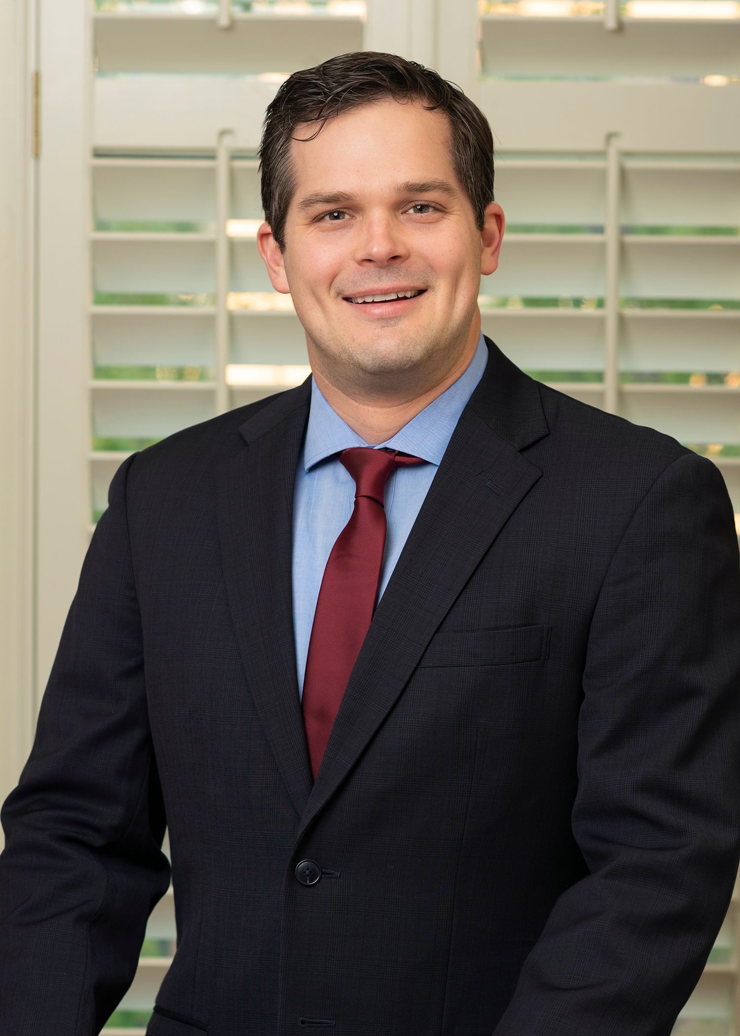 A man in a suit and tie is standing in front of shutters.