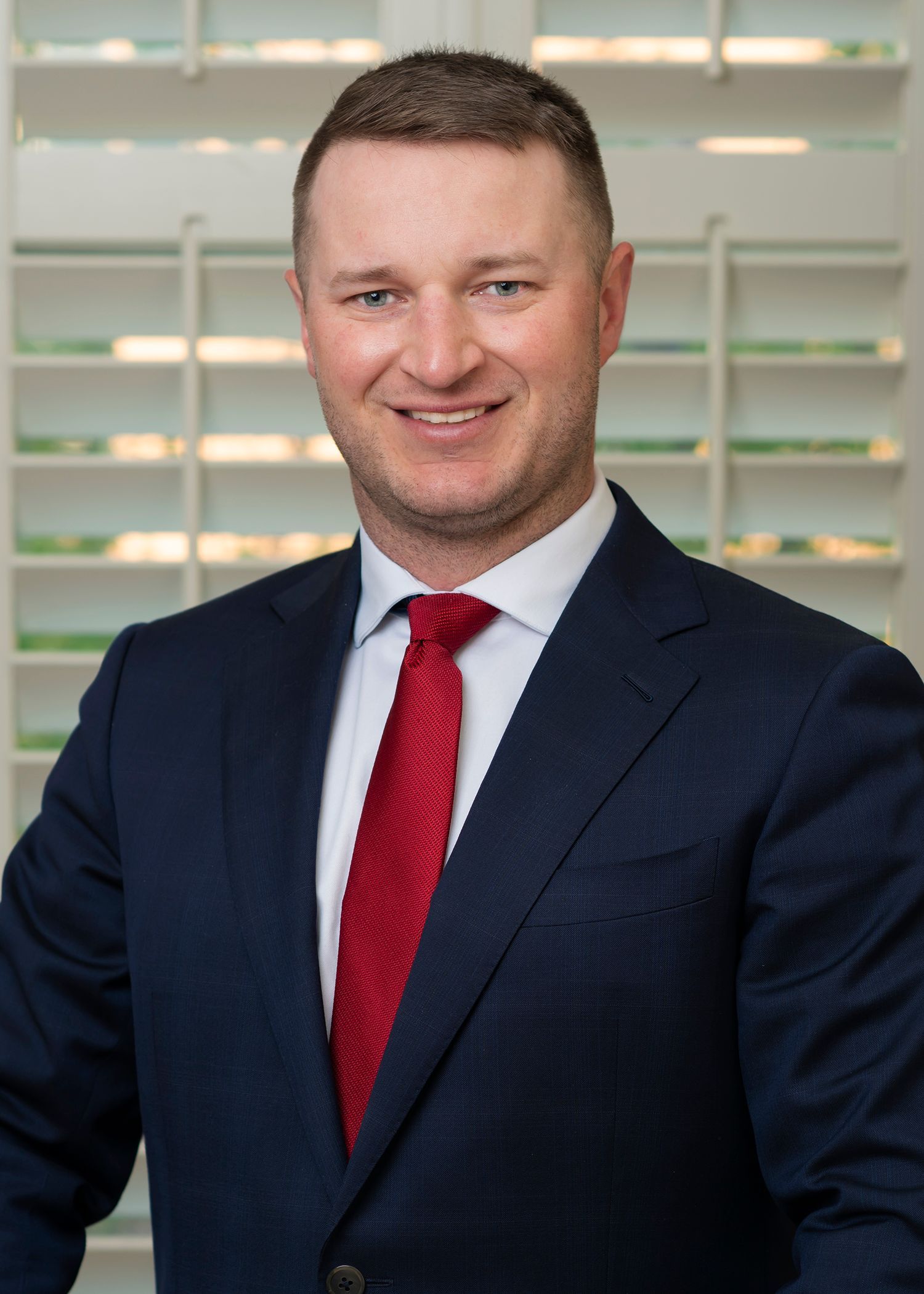 A man in a suit and tie is standing in front of a window.