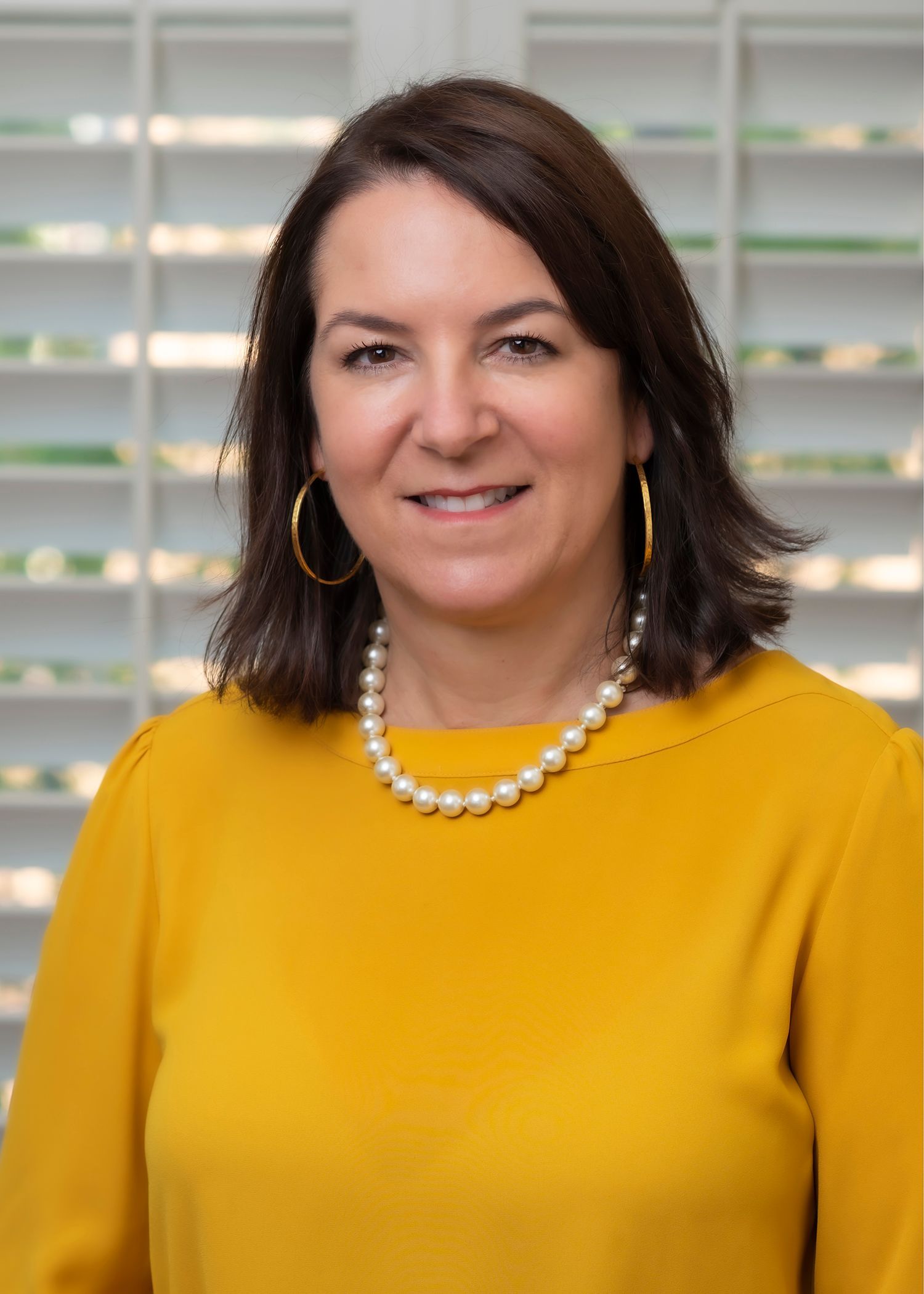Jennifer M Chambliss, Family Law Attorney, wearing a yellow shirt and a pearl necklace is smiling for the camera.