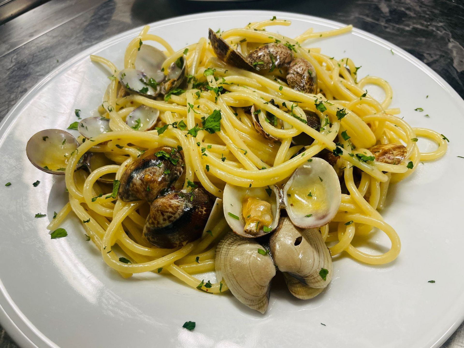 Spaghetti alle vongole, guarniti con prezzemolo, su un piatto bianco.