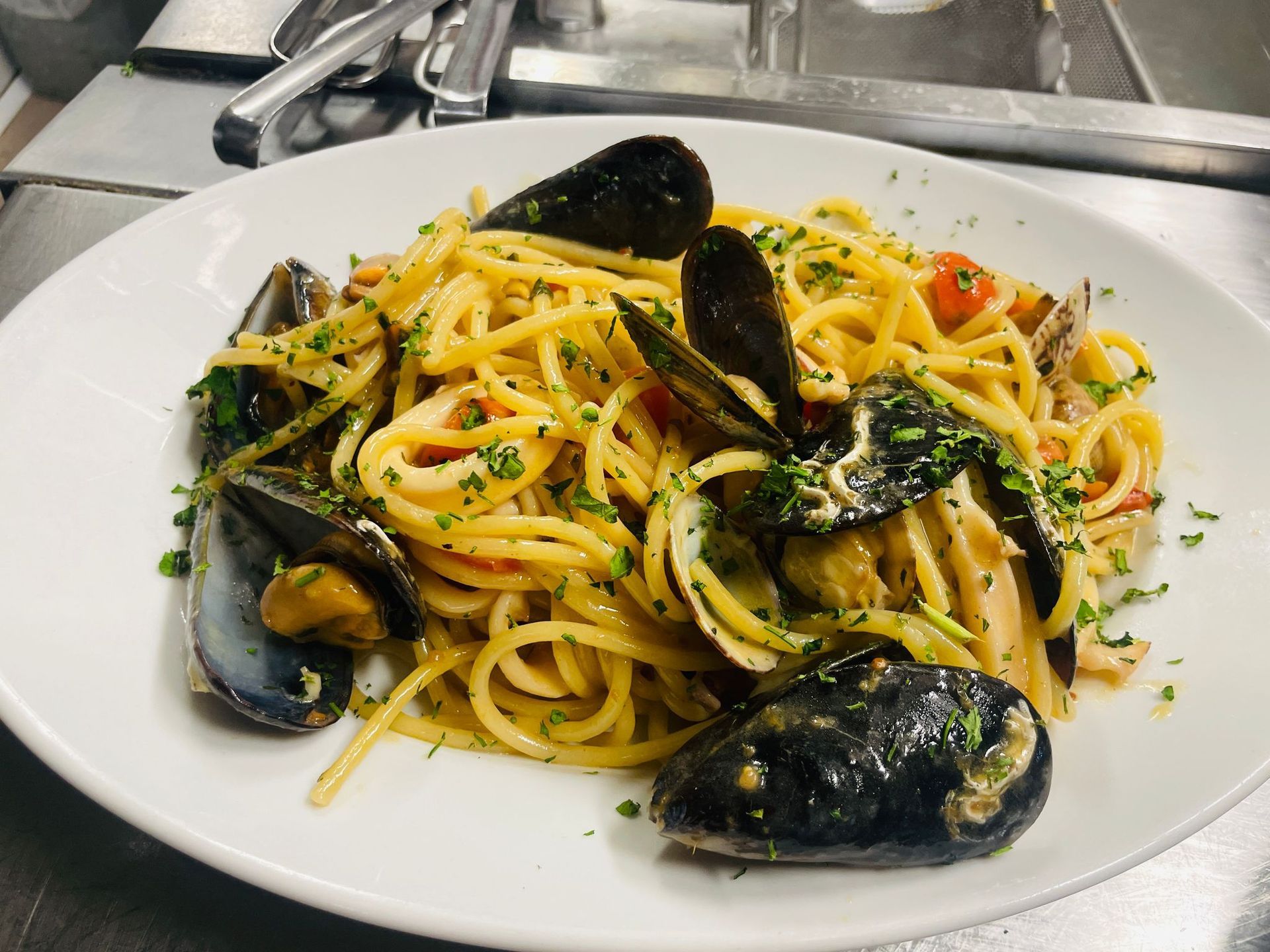 Spaghetti con cozze e vongole su un piatto bianco, guarnito con prezzemolo.