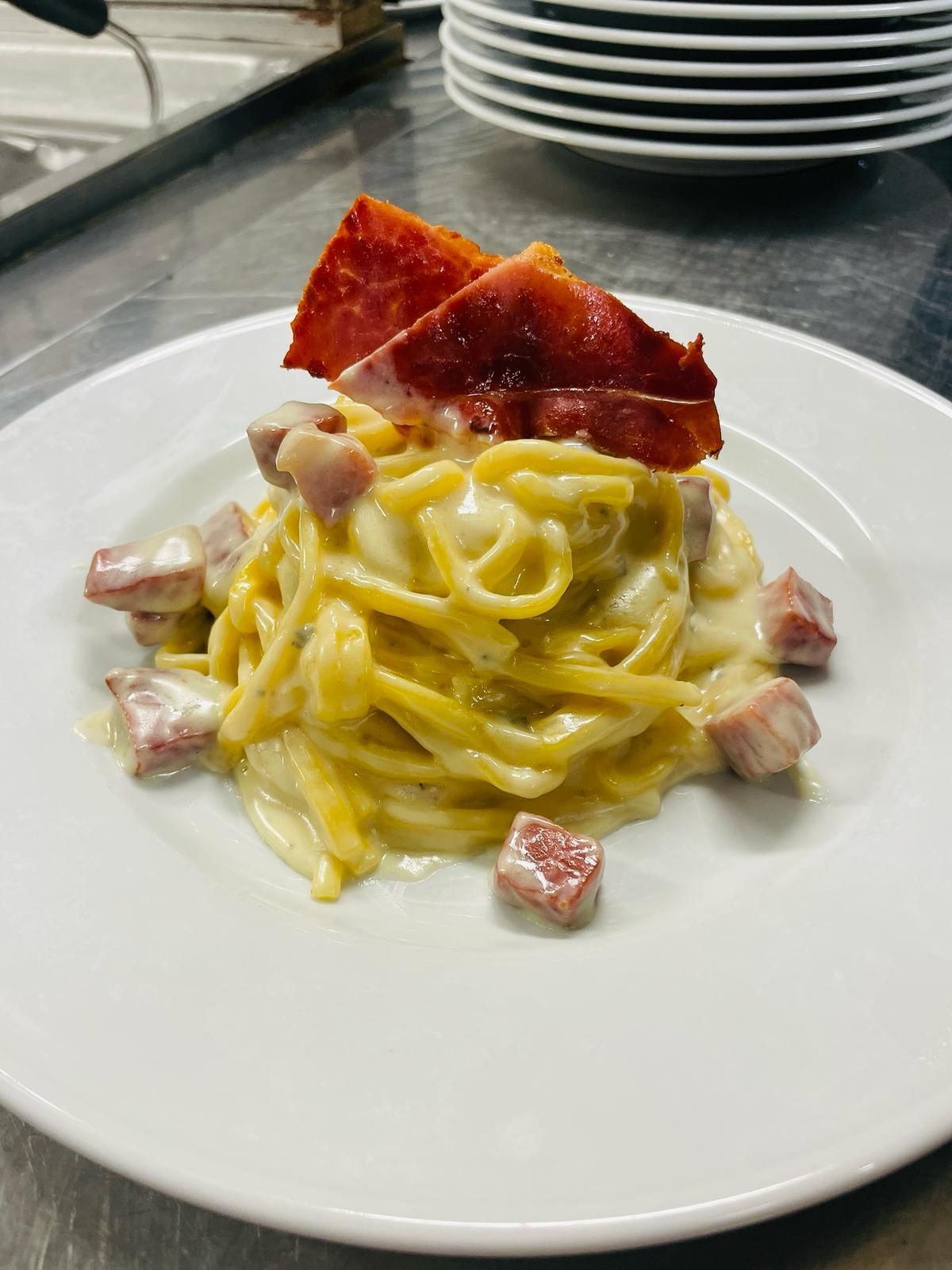 Pasta alla carbonara con pancetta su un piatto bianco, servita in un ambiente da ristorante.